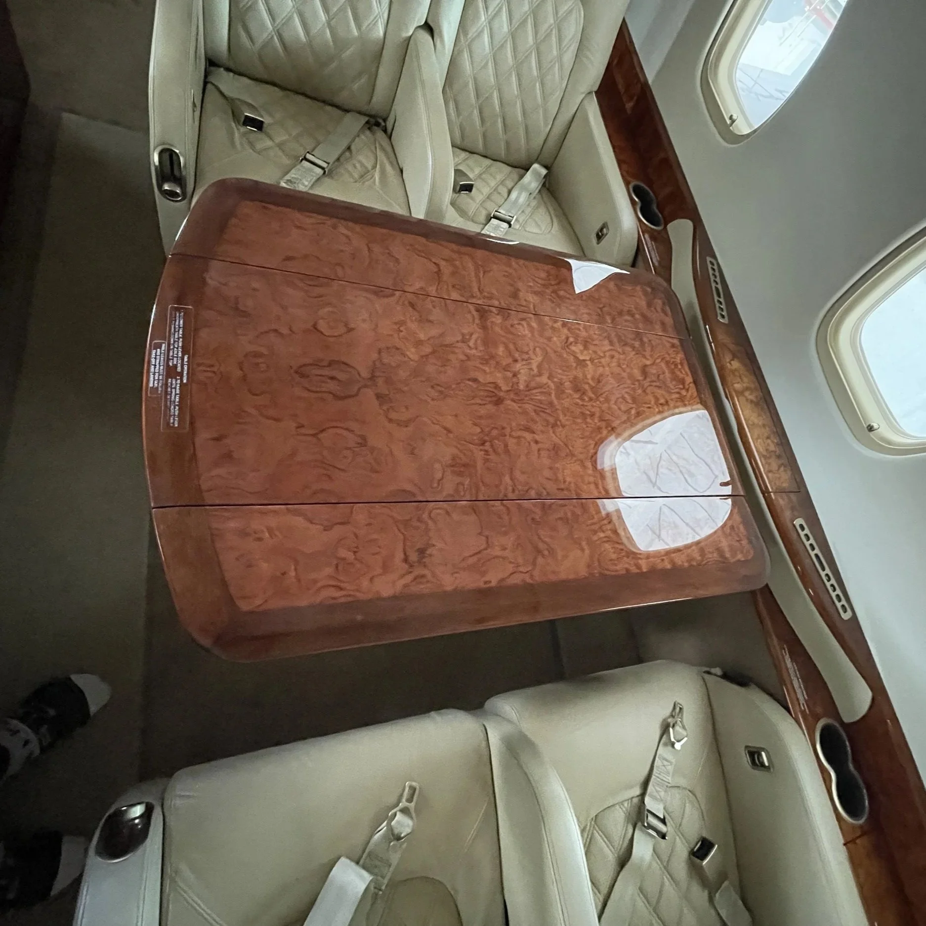 The interior of an aircraft, showing several beige leather seats with seat belts, and a window with outside scenery.