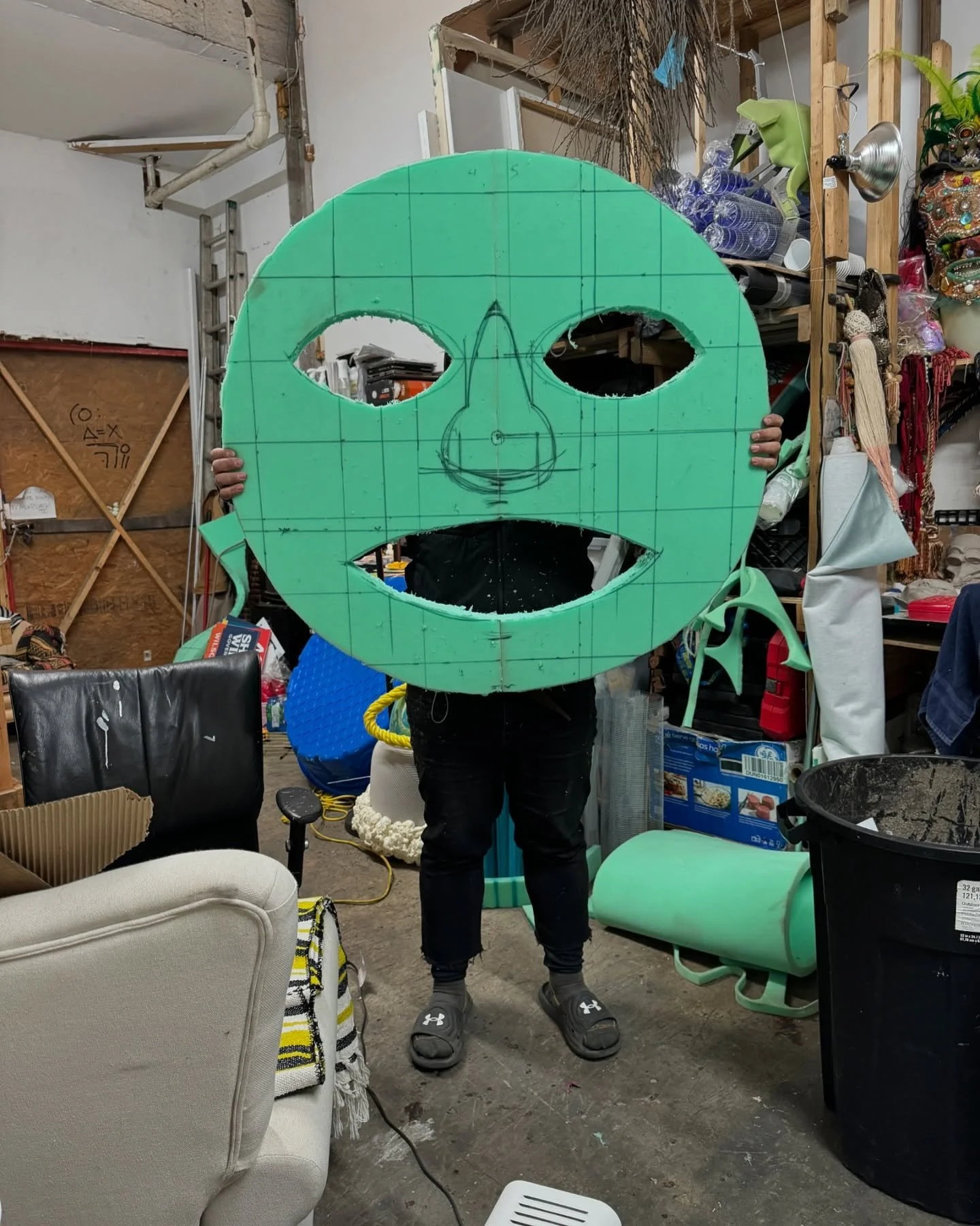 Process view of The Chloe Hotel installation showing a foam mask template beside the finished large outdoor mask mounted on the building.
