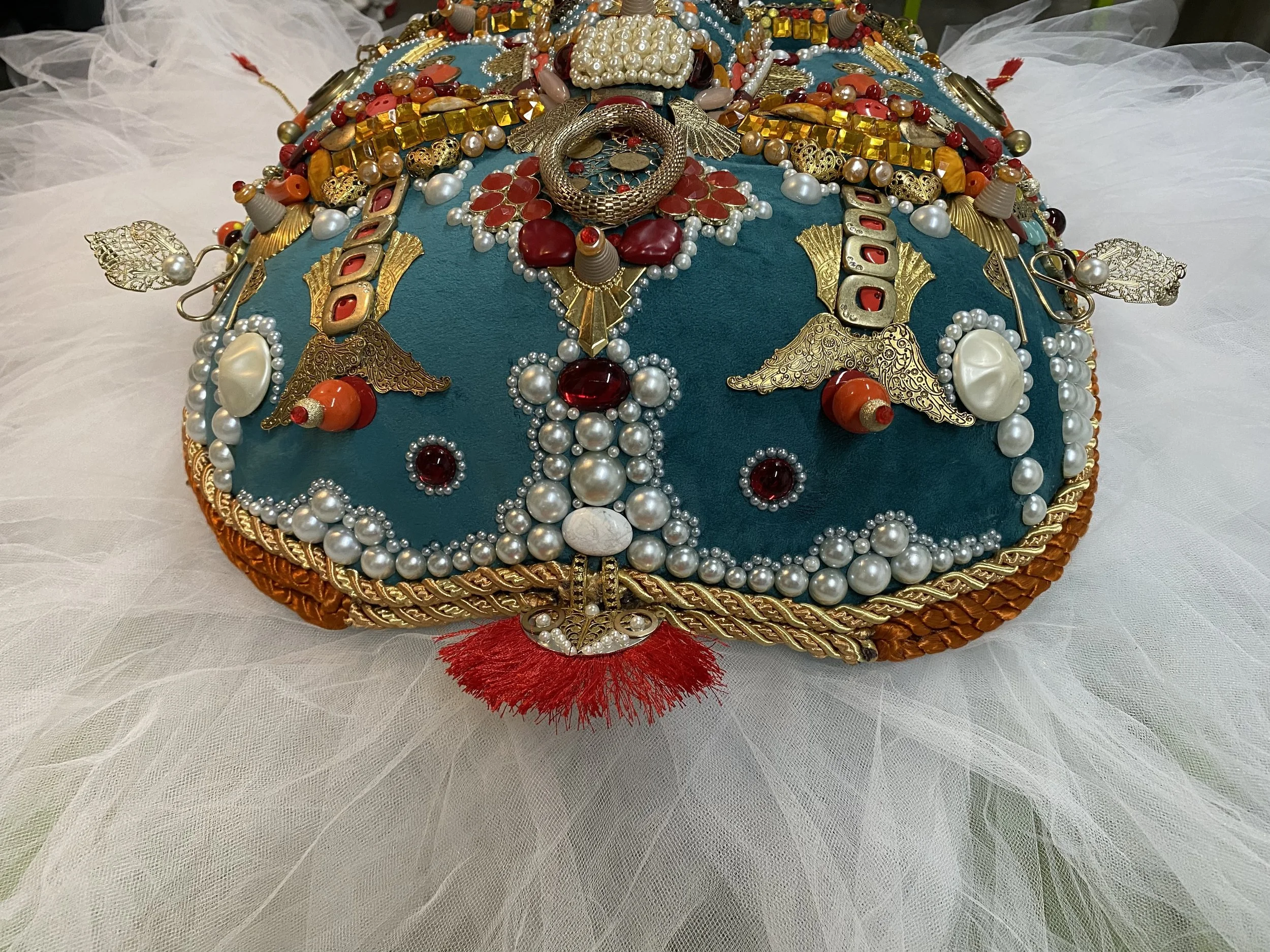 Lower detail of Ajonjolí de Chartres by Basqo Bim showing pearl trim, red crest, gold ornament, and underside construction.