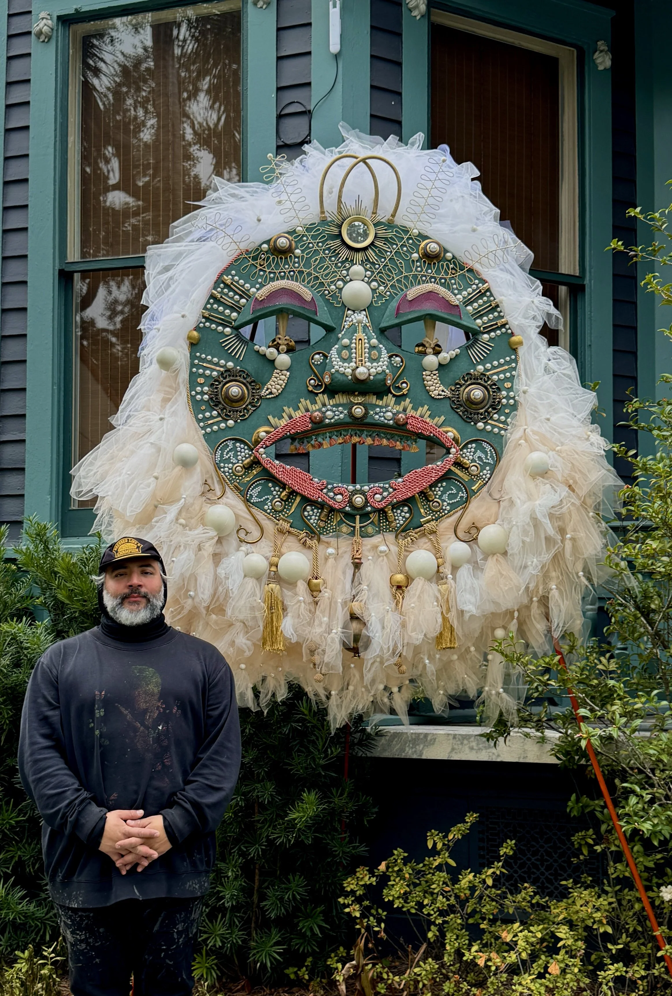 Process view of The Chloe Hotel installation showing a foam mask template beside the finished large outdoor mask mounted on the building.