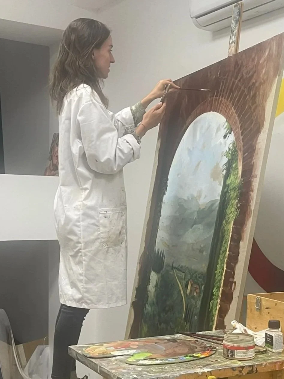 Una mujer que trabaja en un estudio de arte pintando un cuadro grande en un caballete.