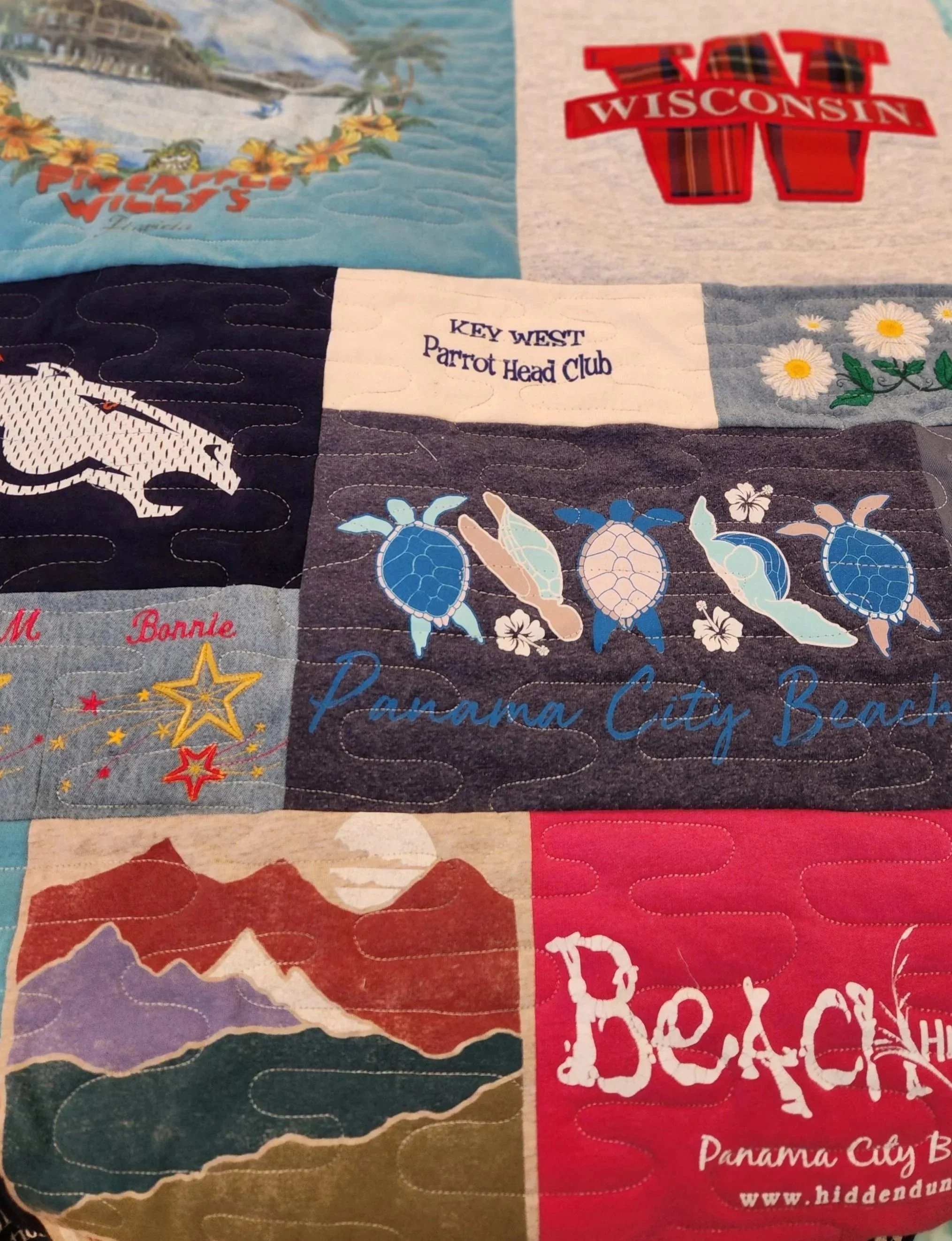 Close-up of a quilt with various travel-themed patches, including images and text for Wisconsin, Panama City Beach, and mountain landscape.