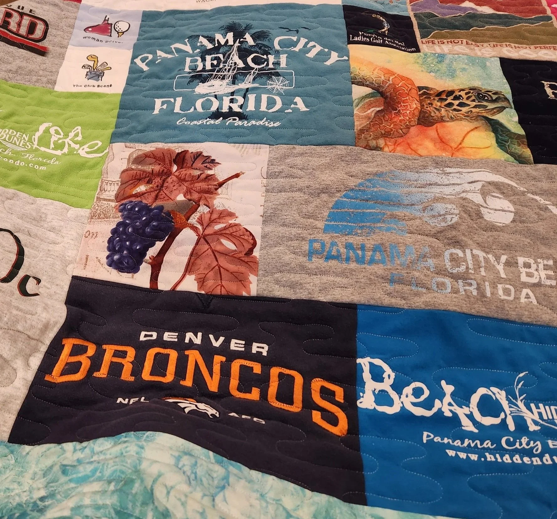 A quilt made of fabric squares, each with different designs and text representing various cities and attractions, including Panama City Beach, Florida, Denver Broncos, and Beach Panama City.