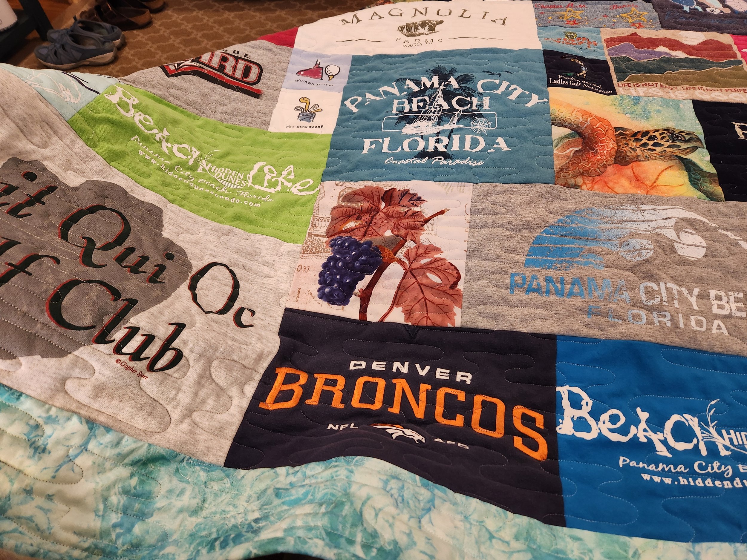 A quilt made of fabric squares, each with different travel-related graphics and text, featuring destinations like Panama City Beach, Florida, and Denver Broncos.