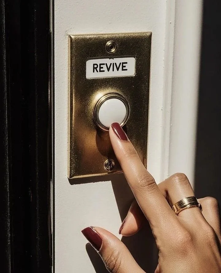 A person with painted nails and a ring pressing a golden doorbell button labeled 'REVIVE'.