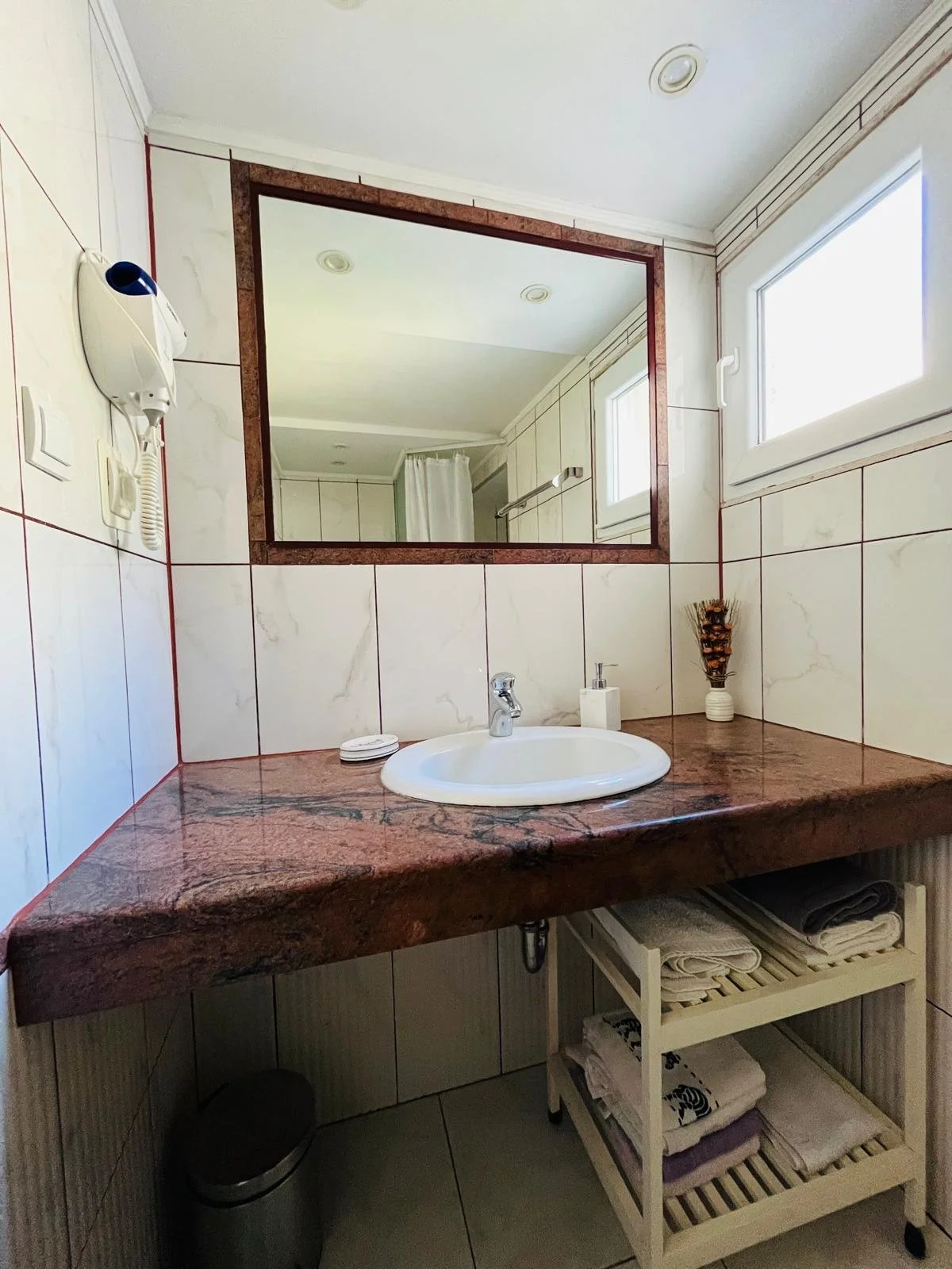 Bathroom with a white sink, a mirror, and a window, with towels stored on a small white shelf.