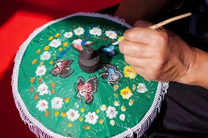 Hand pinning a painted butterfly on a decorative round umbrella with floral and butterfly designs. Thailand Desings