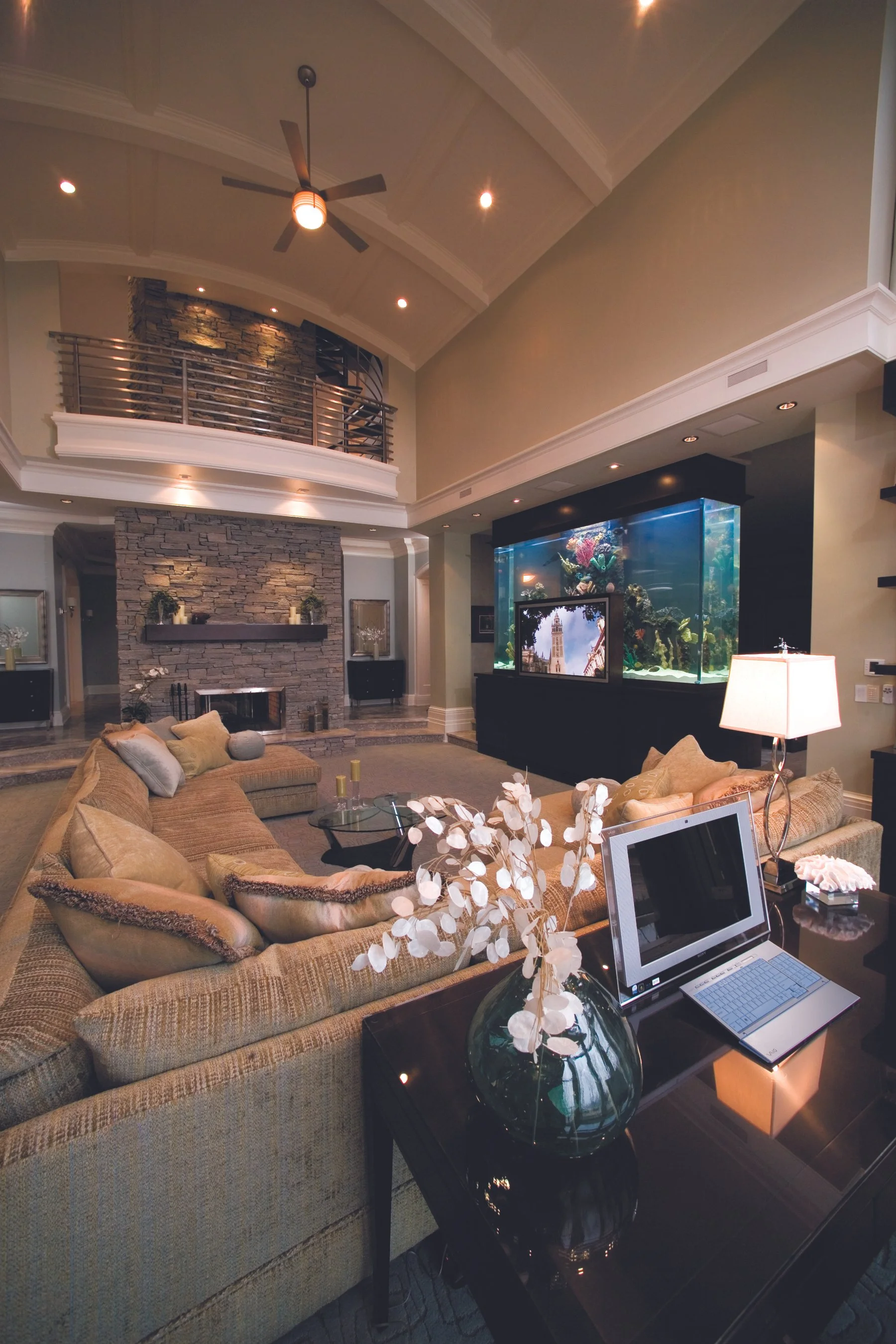 Living room with beige sectional sofa, fireplace with stone surround, large aquarium, TV, and laptop on a side table.