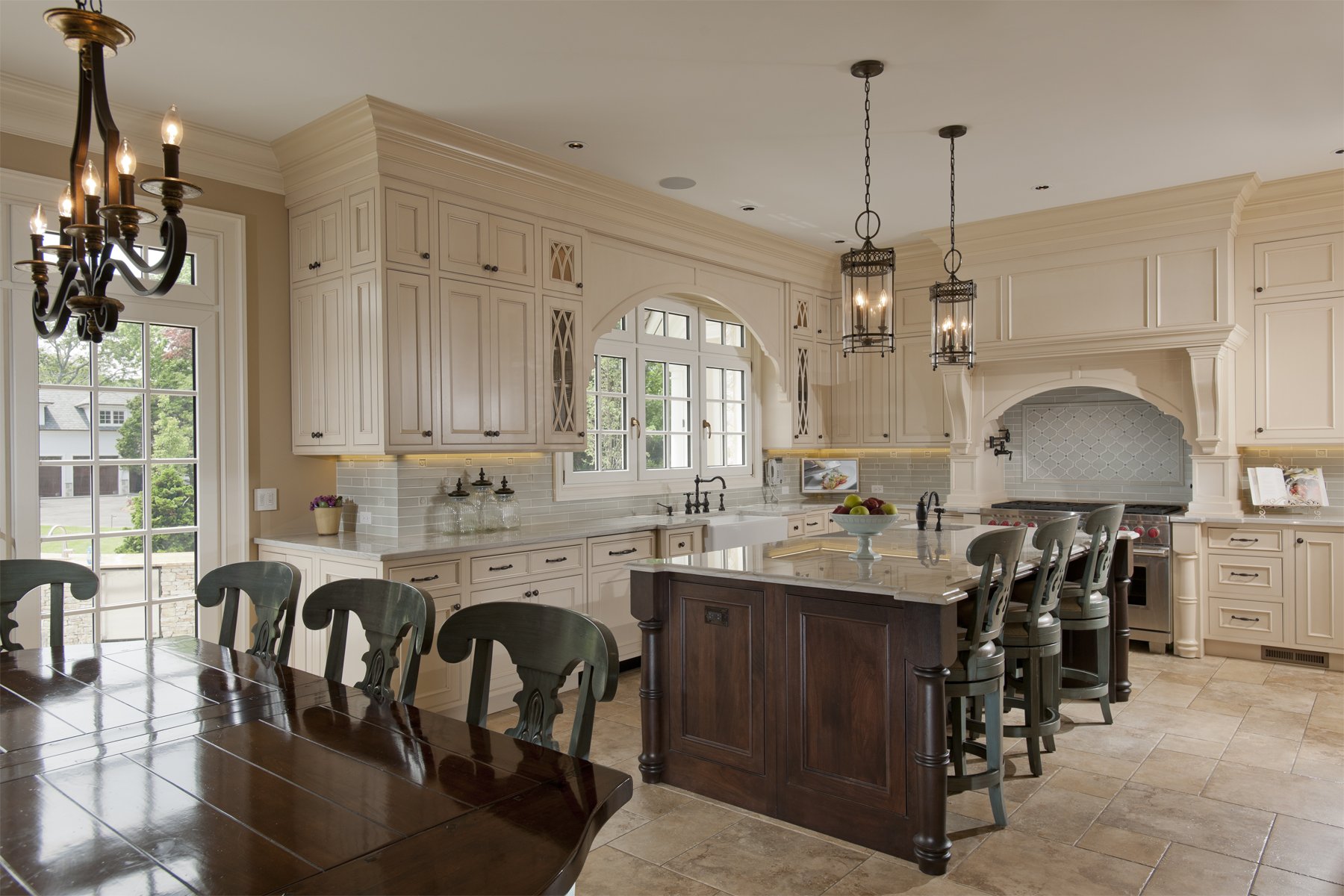 The kitchen features cream-colored cabinets, a central dark wood island with a marble countertop, and a wooden dining table with chairs. There are three pendant lights hanging over the island and a chandelier over the dining table. The kitchen has a 