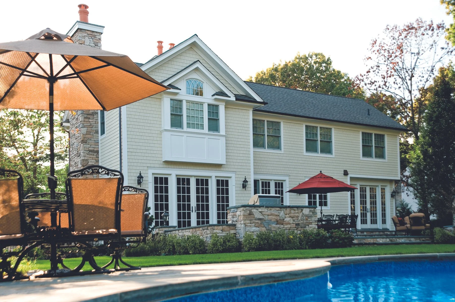 Backyard view with a house, a swimming pool, and patio furniture including umbrellas, chairs, and tables.