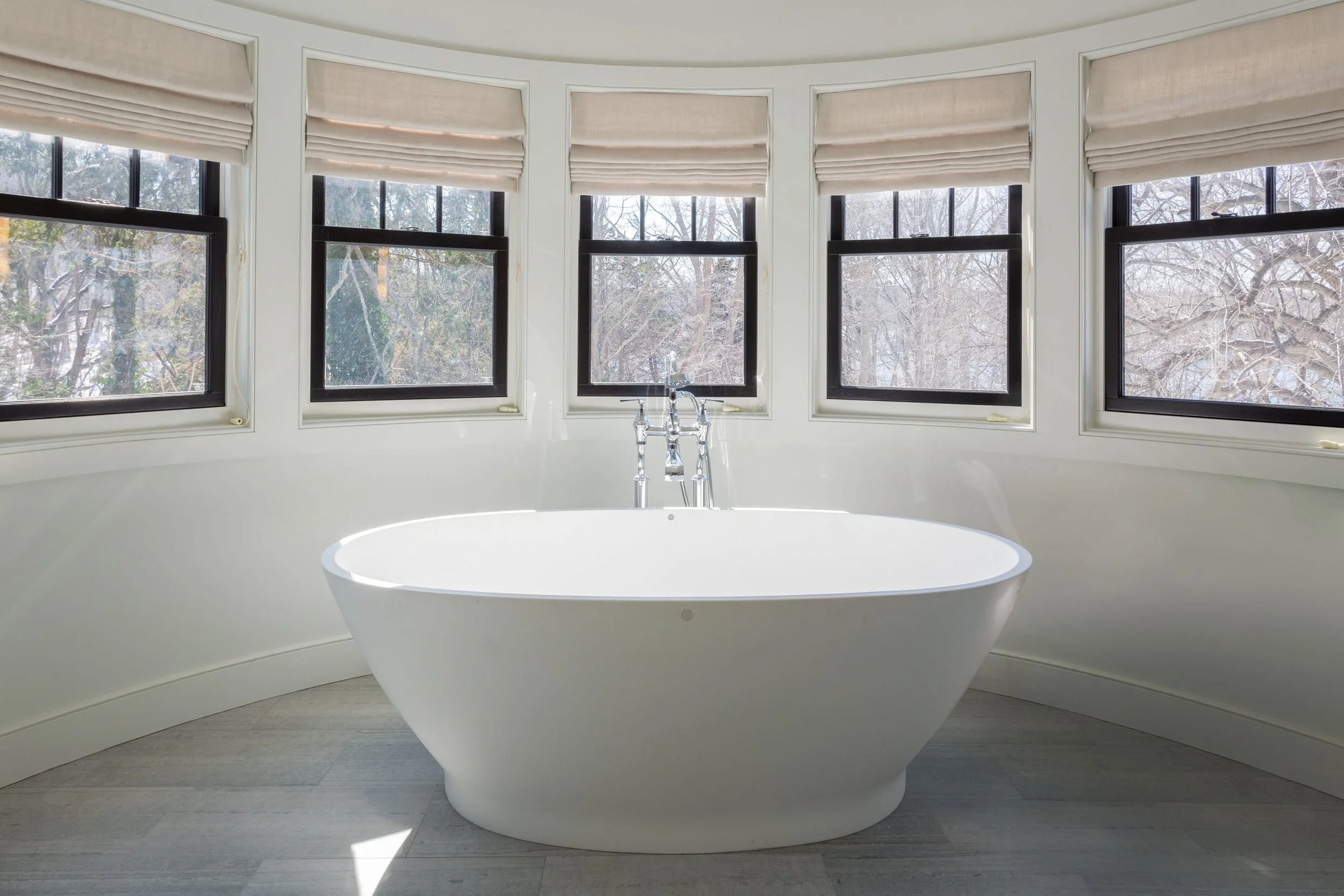 White freestanding bathtub in a bright bathroom with five windows showing a winter scene with trees and snow