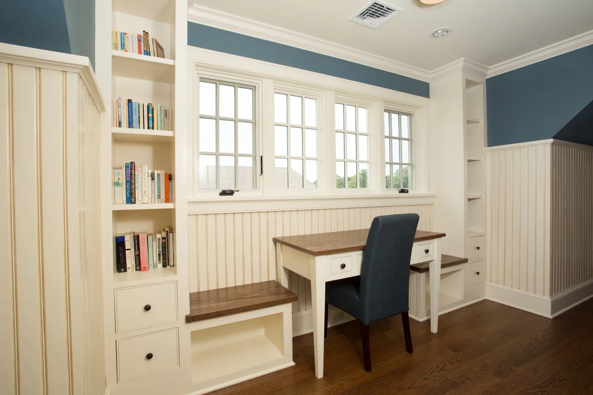 A small home office nook with a desk, chair, built-in bookshelves on either side, and a large window with multiple panes.