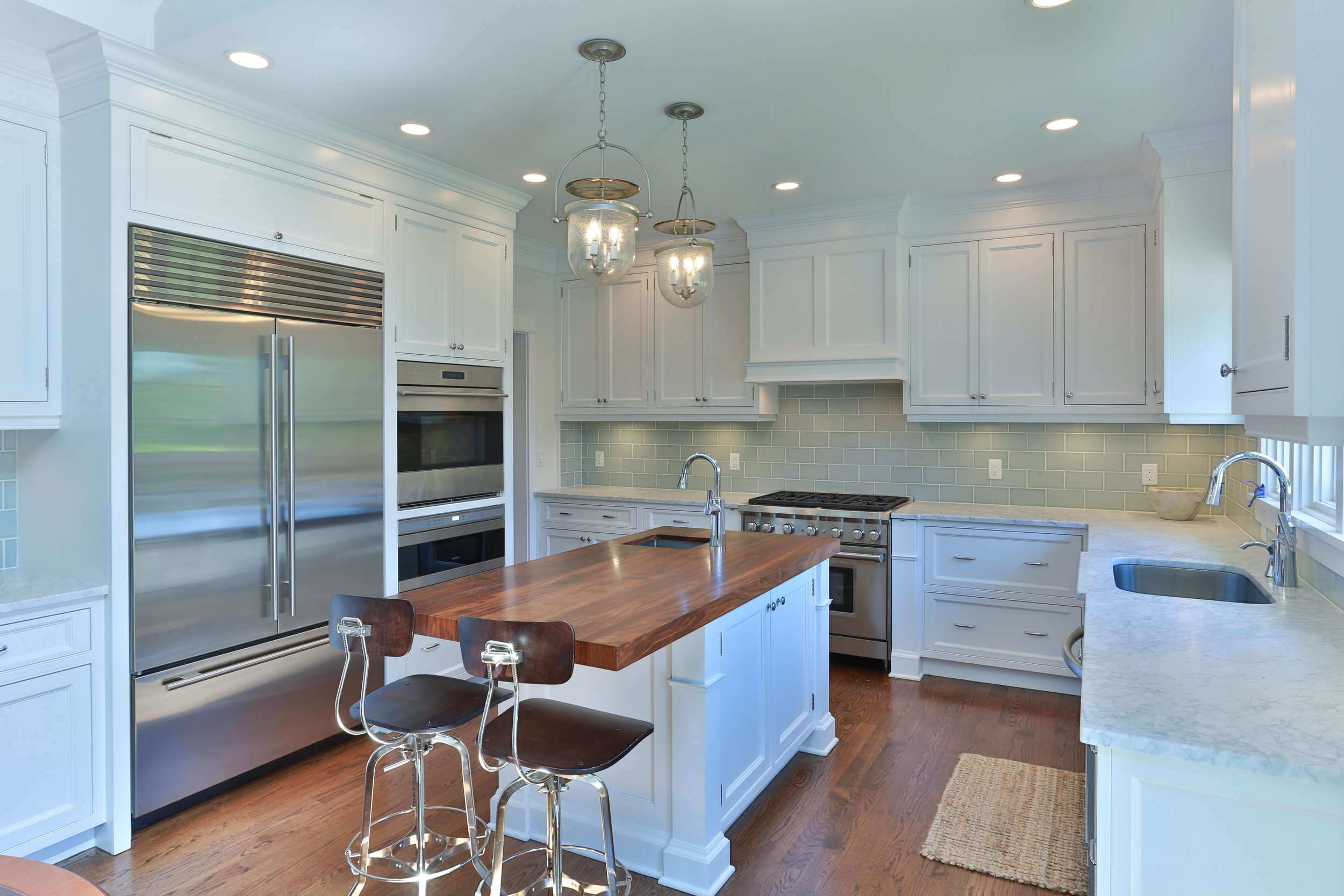 Modern kitchen with white cabinets, stainless steel appliances, a wooden island with seating, and a green tiled backsplash.