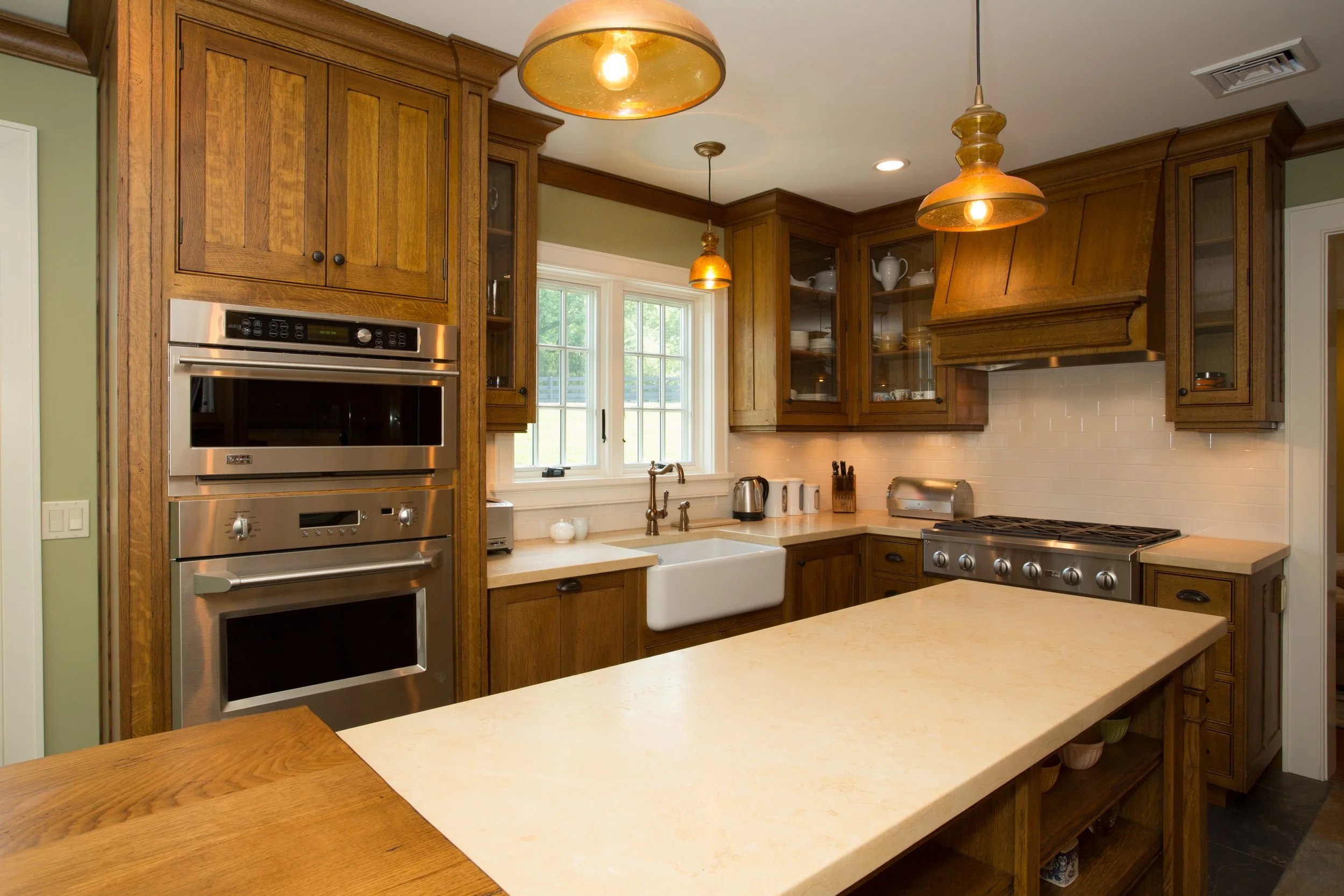 Kitchen with wooden cabinets, stainless steel appliances, a white farmhouse sink, and a beige countertop with pendant lighting.