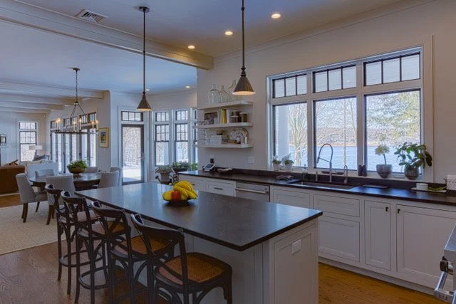 Spacious kitchen with large central island, white cabinetry, pendant lighting, and large windows overlooking an outdoor view.