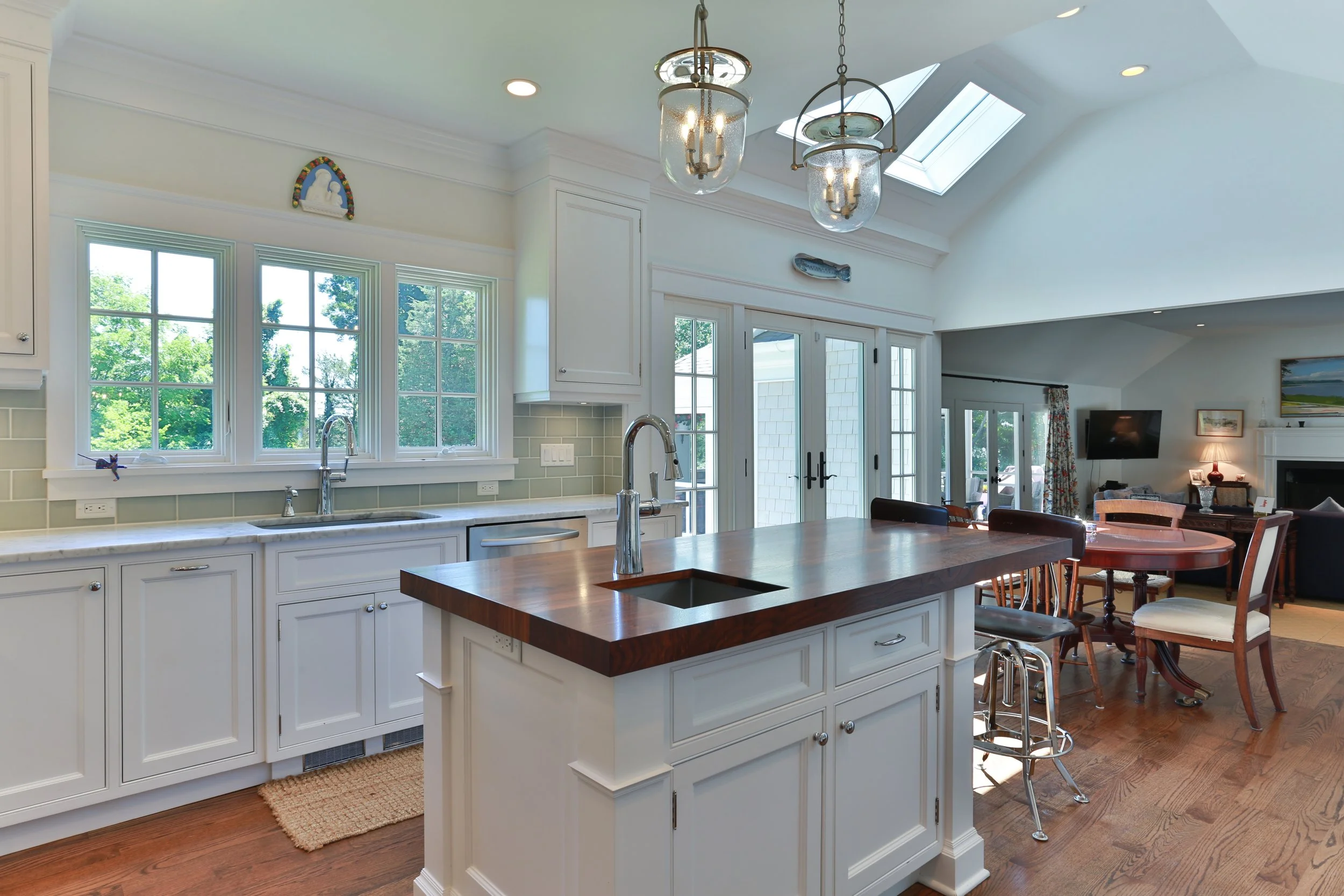 Bright kitchen with white cabinets, an island with a dark wood countertop, multiple windows, a skylight, and a dining area with a round table and chairs.