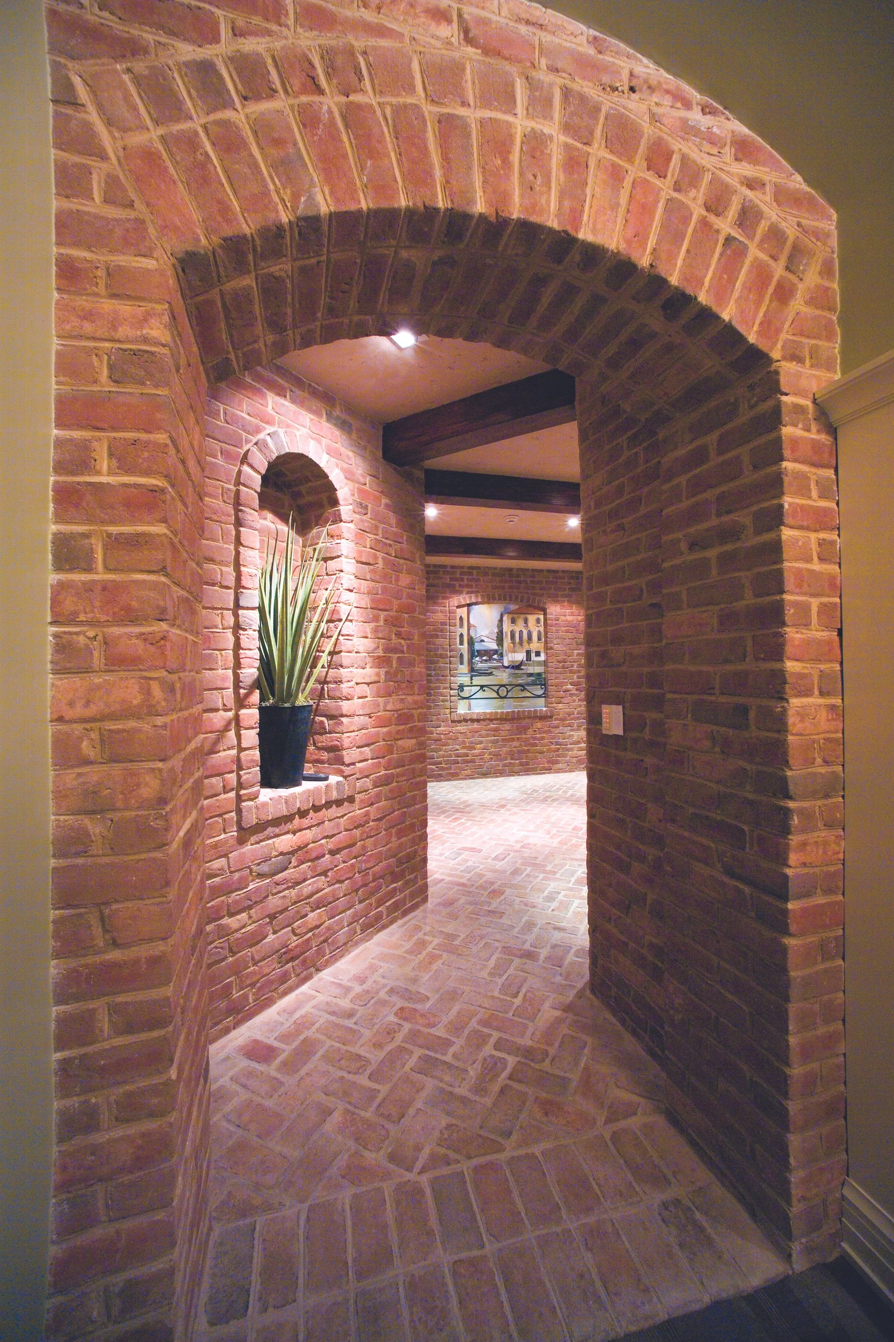 Brick hallway with arched doorways and small wall alcove with potted plant.