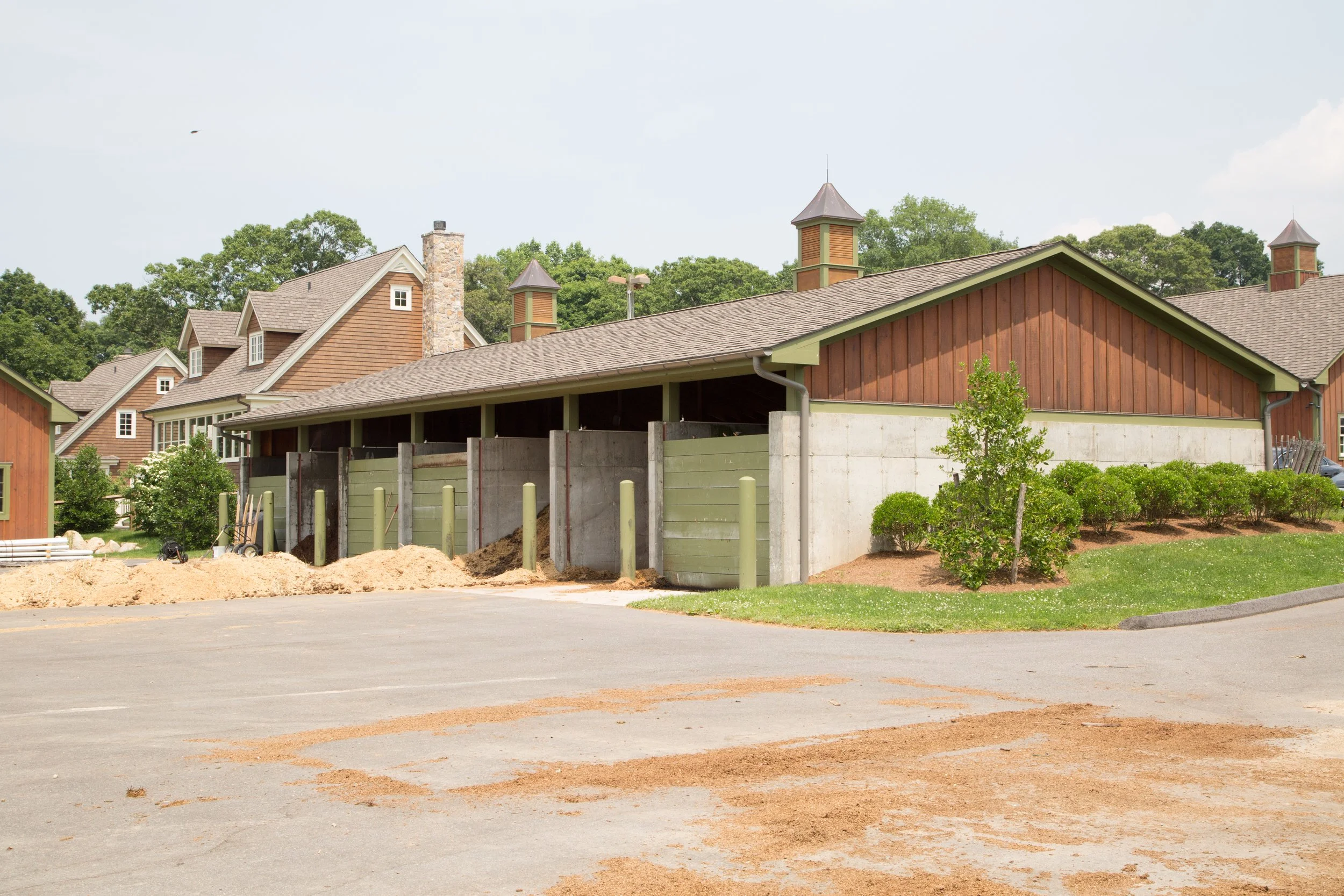 Construction site with a building under renovation, piles of dirt, and wooden barriers, surrounded by residential houses and greenery.