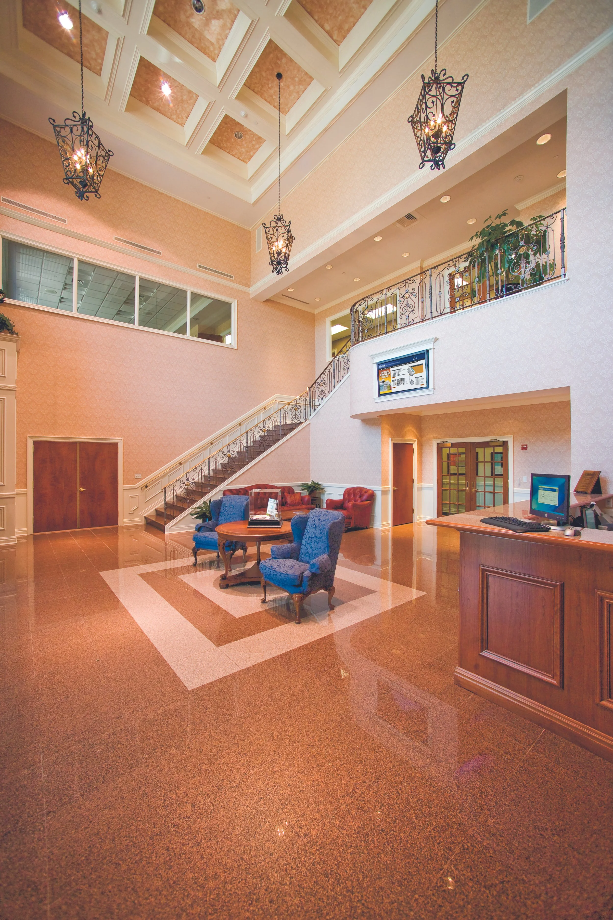 Hotel lobby with a reception desk, colorful chairs, a staircase, and hanging lantern-style light fixtures.