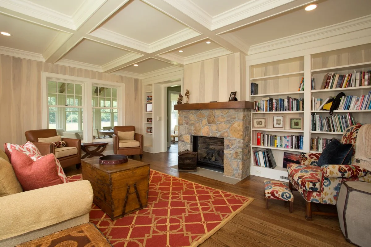 Living room with beige sofa, armchairs, a stone fireplace, built-in bookshelves, hardwood floors, and large windows.