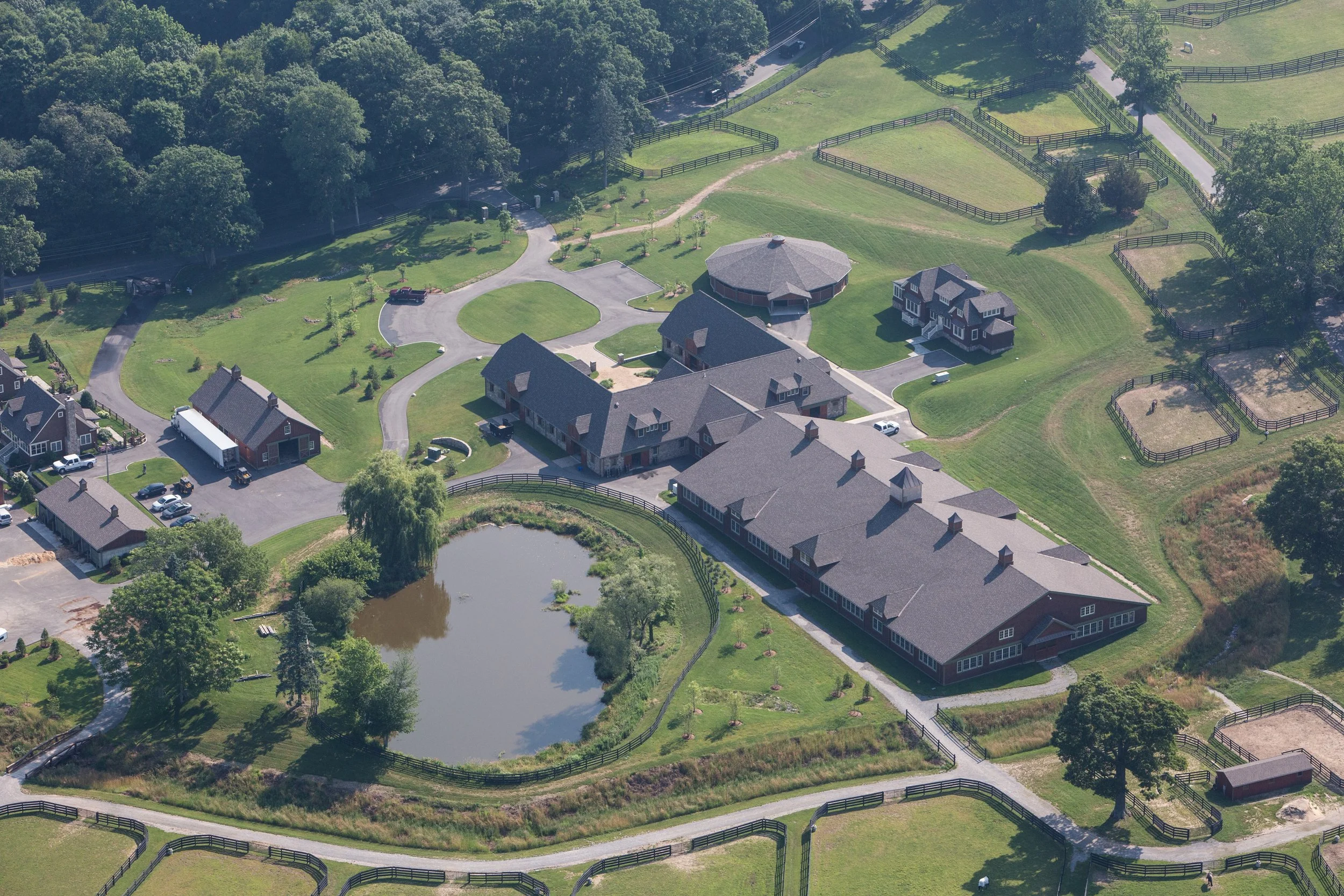 Aerial view of a large estate with multiple buildings, a pond, and fenced paddocks on lush green land.