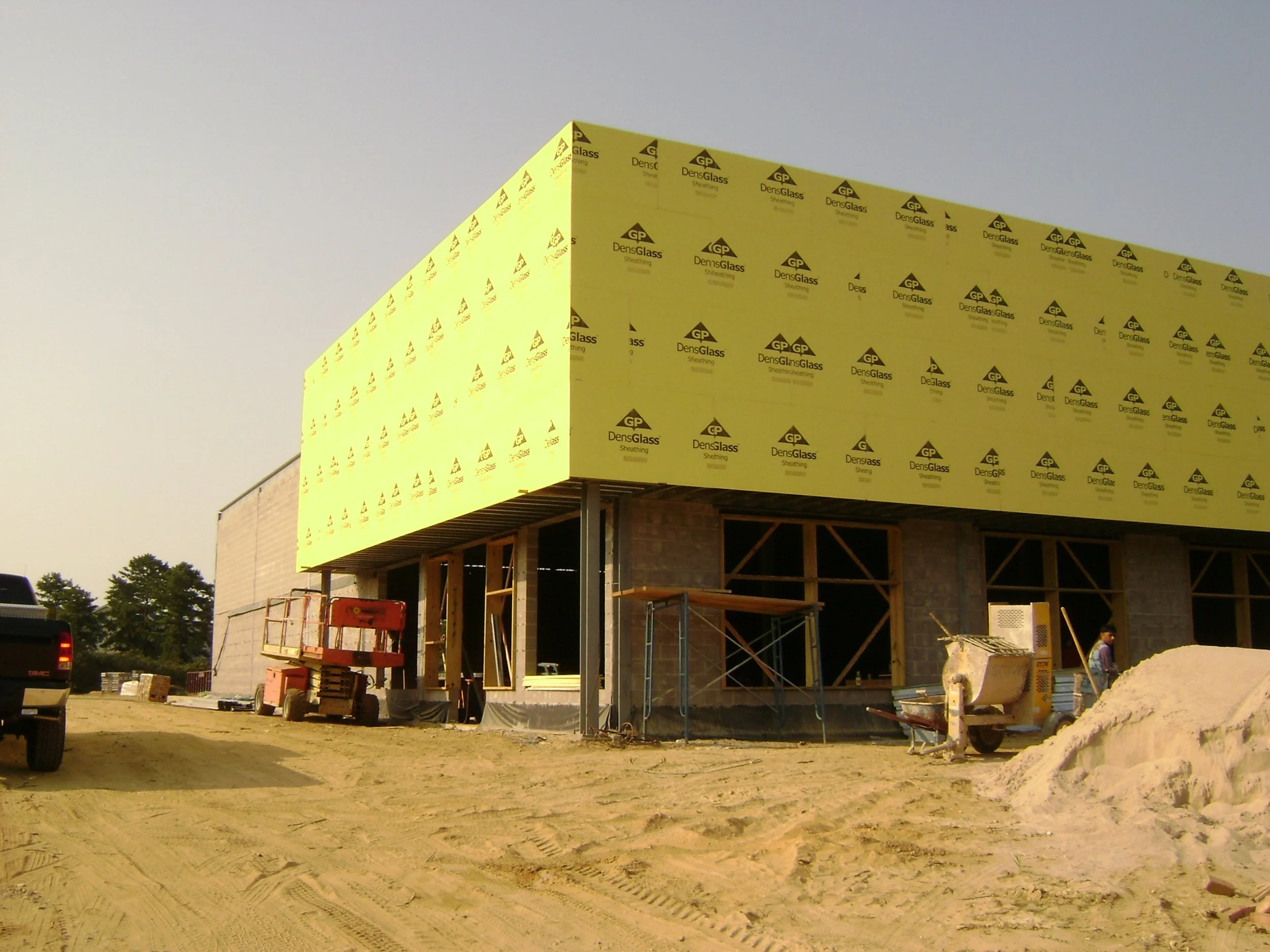 Construction site with partially built building, yellow insulation panels, construction equipment, and a worker.