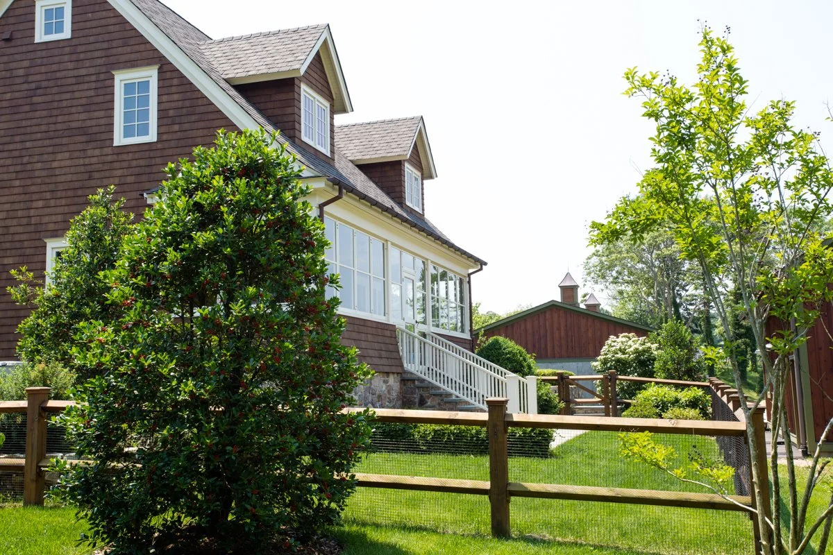 View of a well-maintained backyard with a multi-story house, green bushes, trees, and a wooden fence