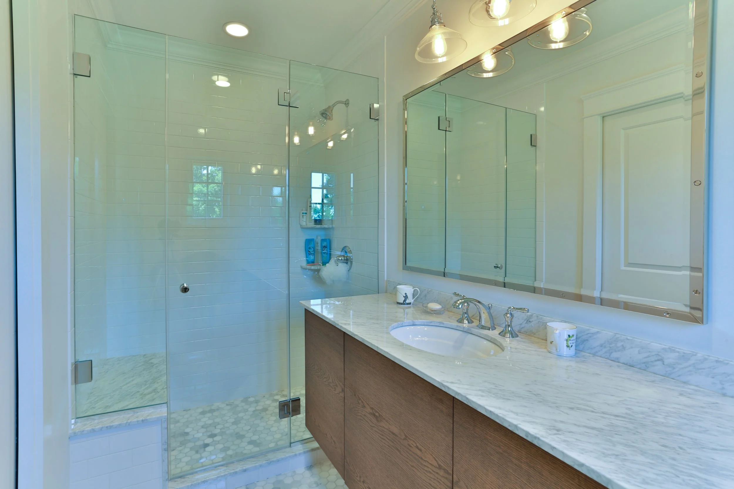 Modern bathroom with glass-enclosed shower, white subway tile walls, a marble countertop vanity with a sink, and a large mirror.