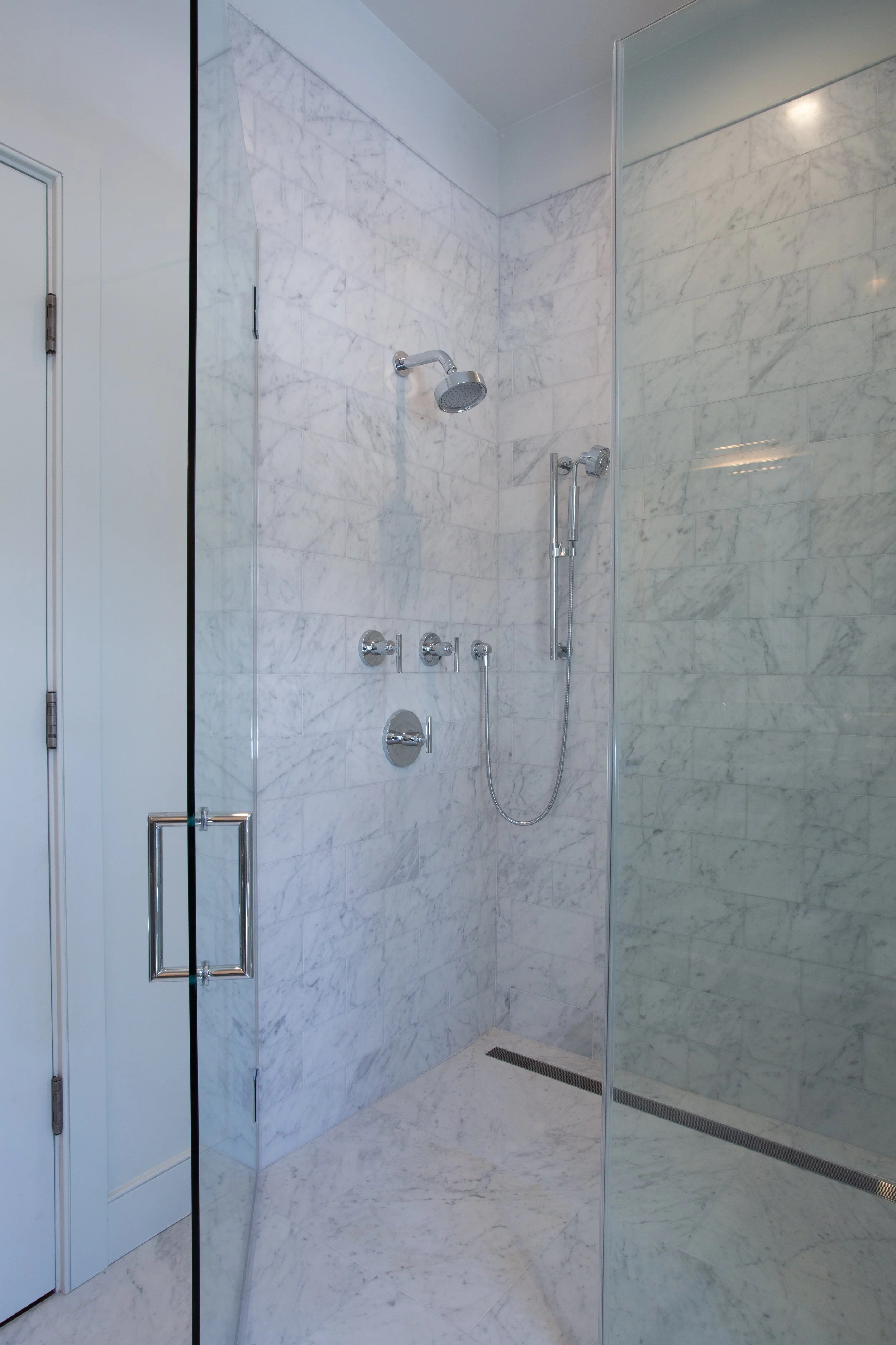 A modern marble shower with a glass door, chrome fixtures, and a handheld showerhead.