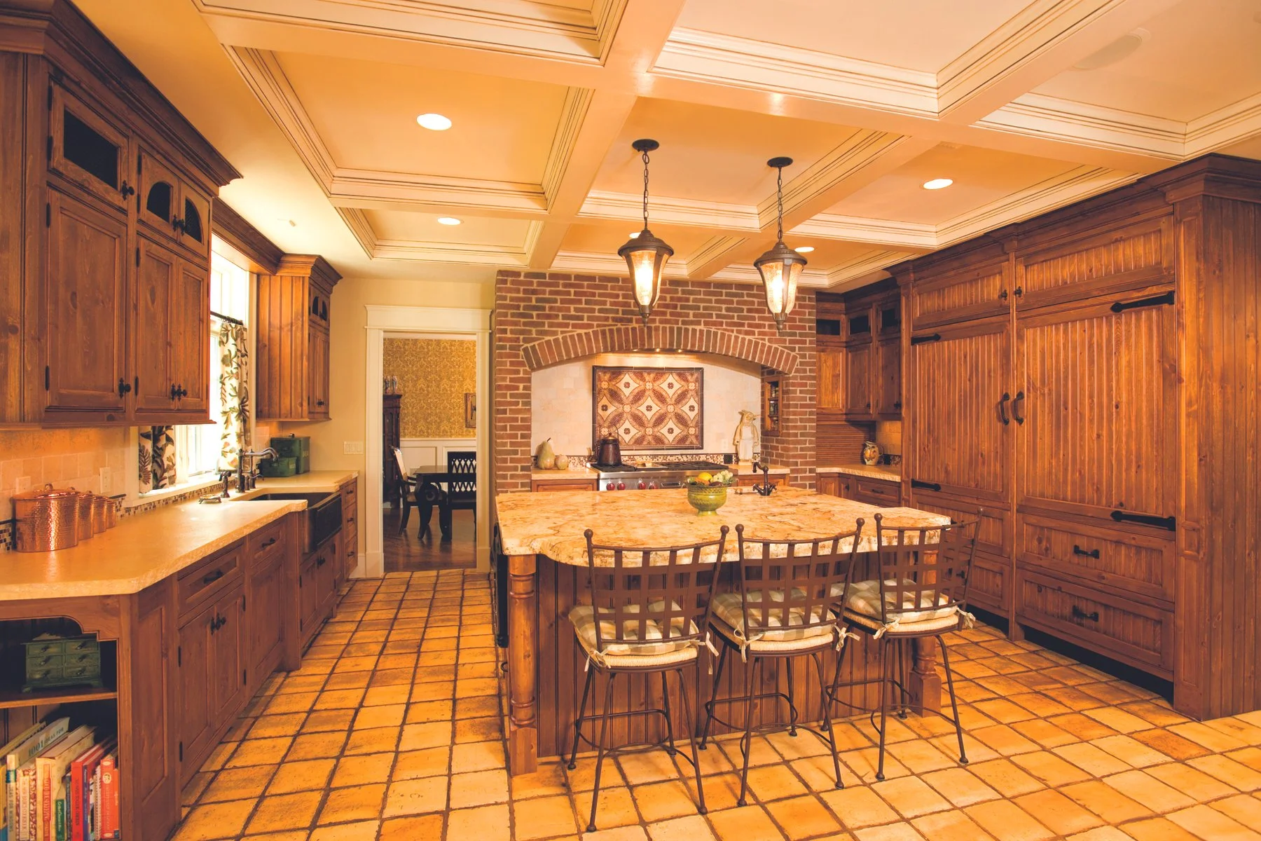 Kitchen with wooden cabinets, brick arch over stove, tiled flooring, island with chairs, and two hanging pendant lights.