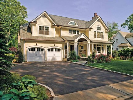 A large two-story house with a front porch, attached garage, and well-maintained landscaping surrounded by trees.