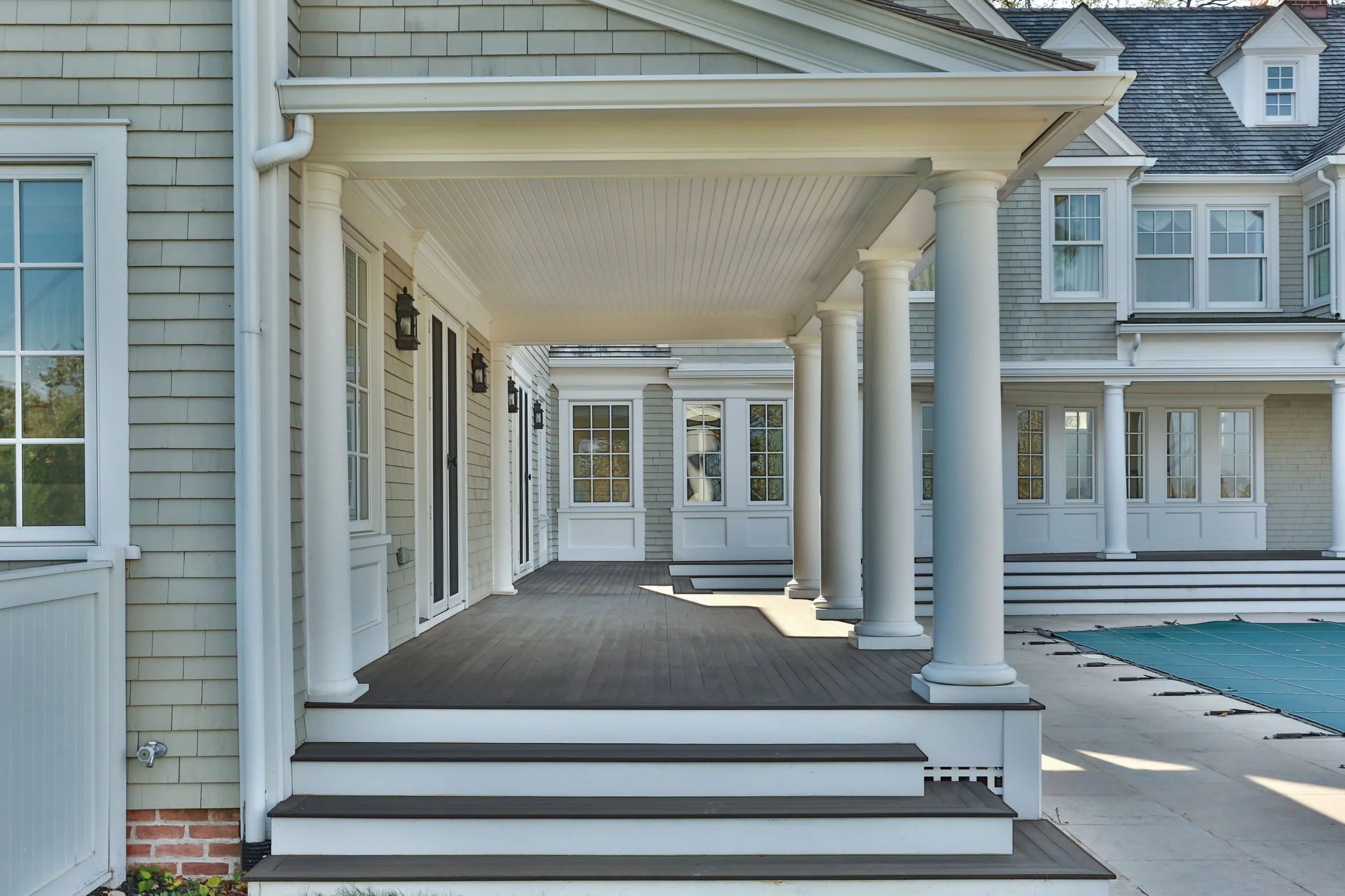 Back porch with white columns, steps leading up, and a screened door in a suburban house.
