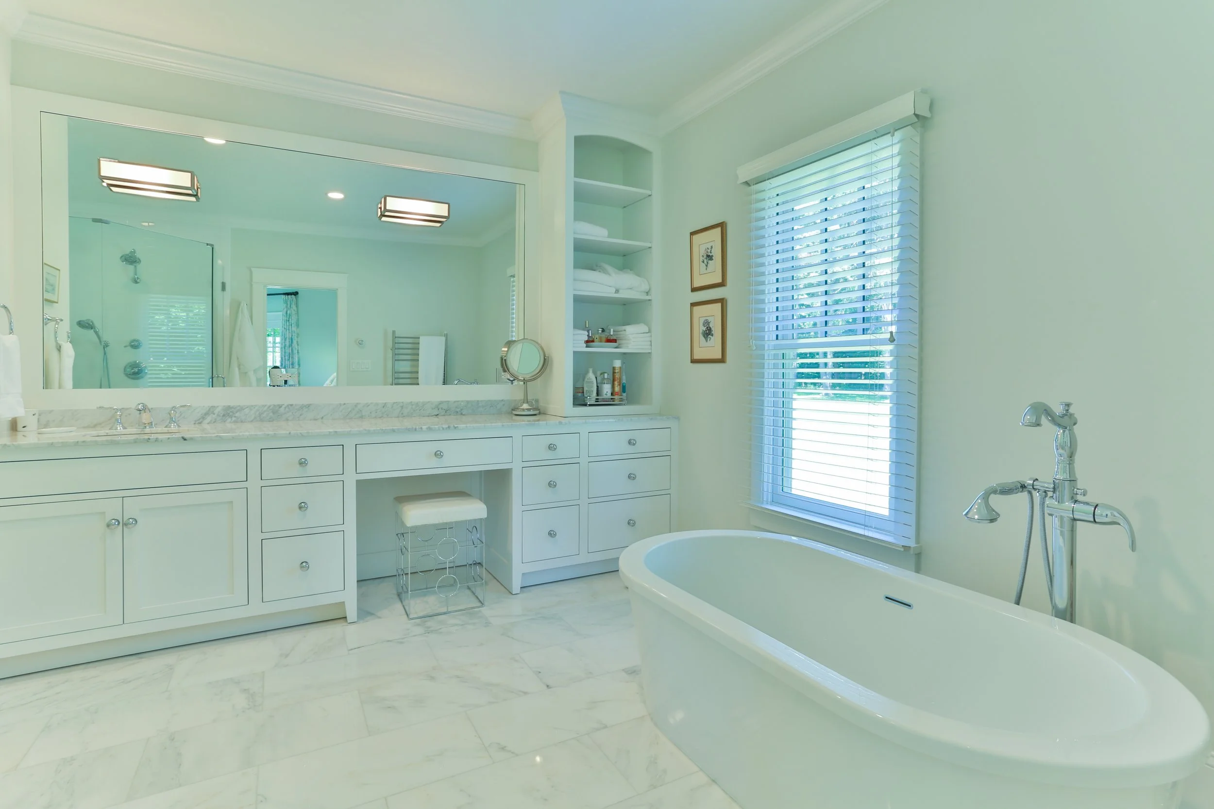 Bright bathroom featuring a white bathtub, a large mirror above a marble countertop, open shelves with towels, a window with blinds, and a walk-in shower with glass doors.