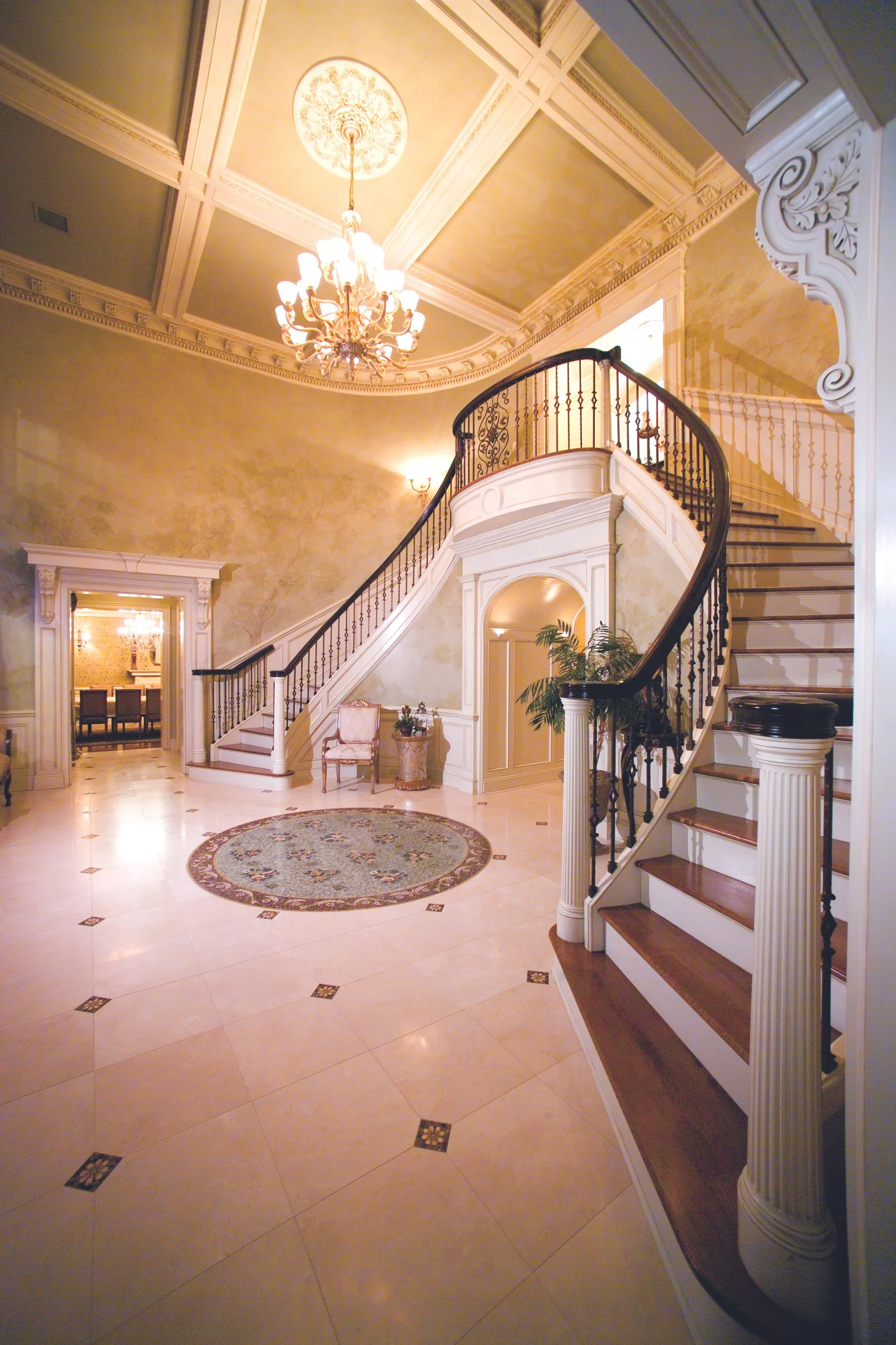 Elegant grand foyer with staircase, chandelier, and ornate ceiling details.