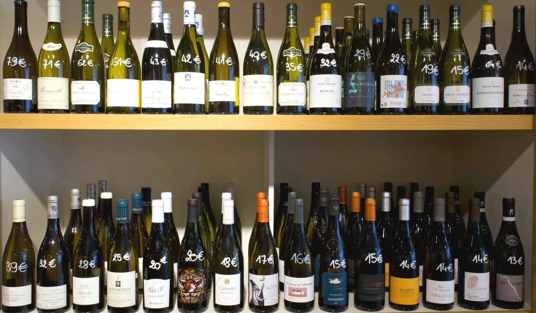 Rayonnage de bouteilles de vin avec prix inscrits en blanc sur chaque bouteille, deux niveaux de bouteilles.