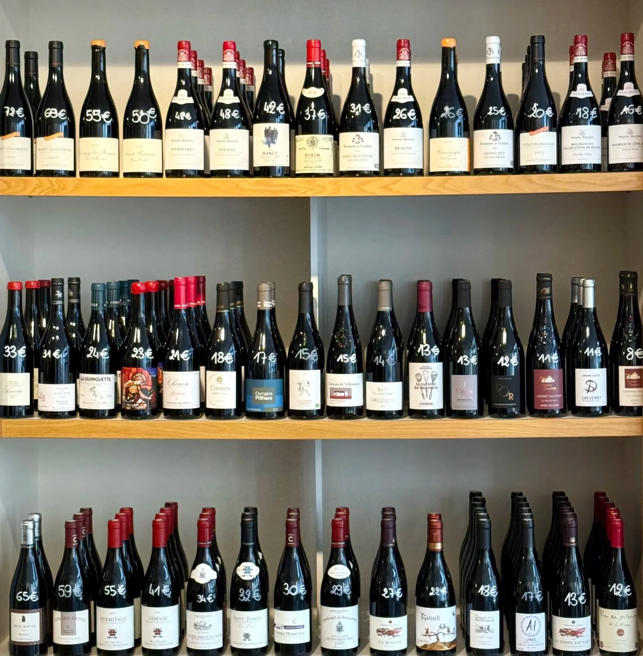 Une étagère remplie de bouteilles de vin avec des prix écrits en blanc sur chaque bouteille.