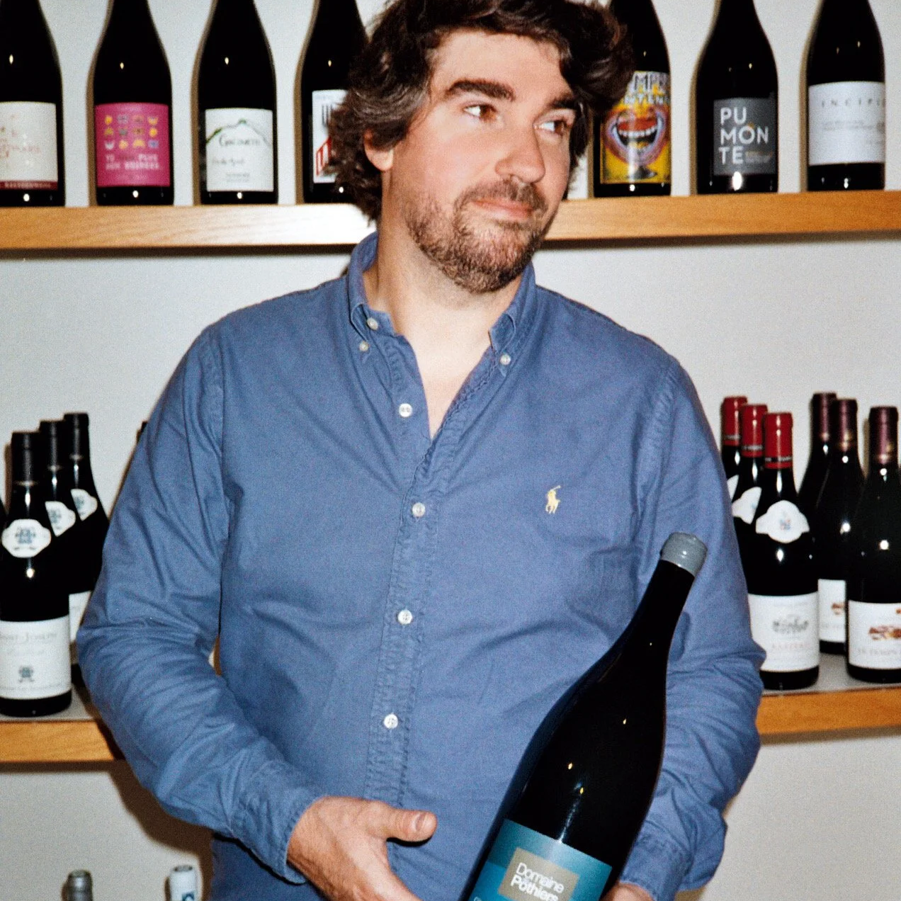 Un homme tient une bouteille de vin devant une étagère de bouteilles de vin dans une wine shop.