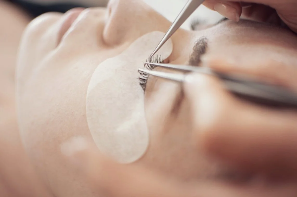 Person receiving eyelash extension procedure with tools near the eye.