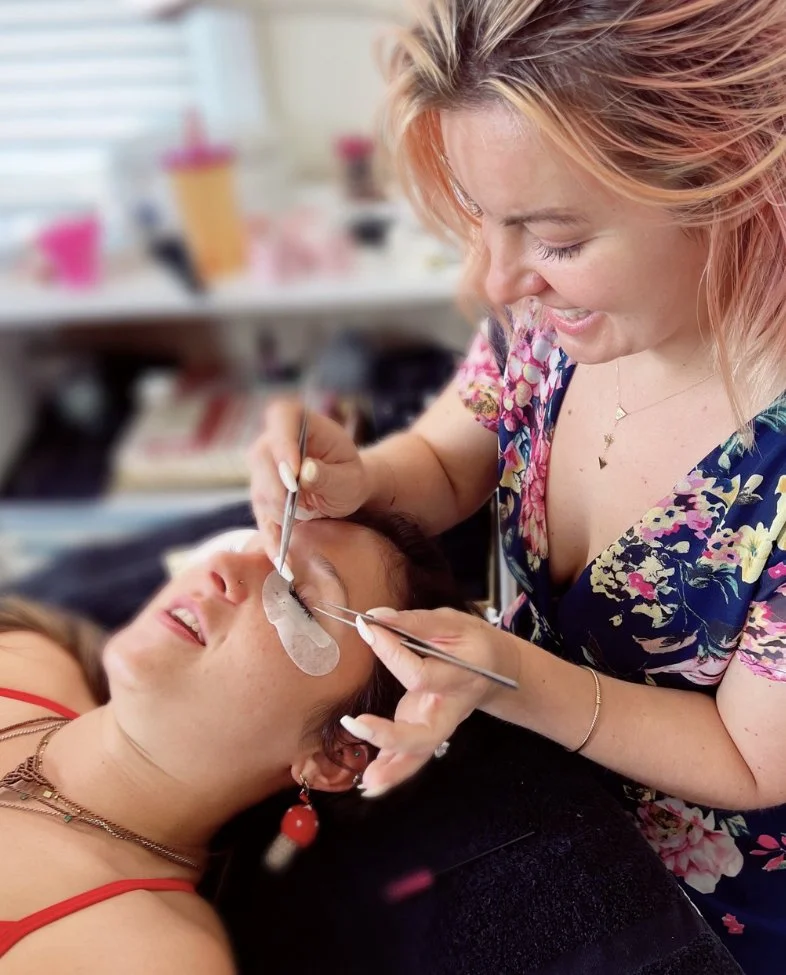 A woman receiving eyelash extensions from a technician in a beauty salon.
