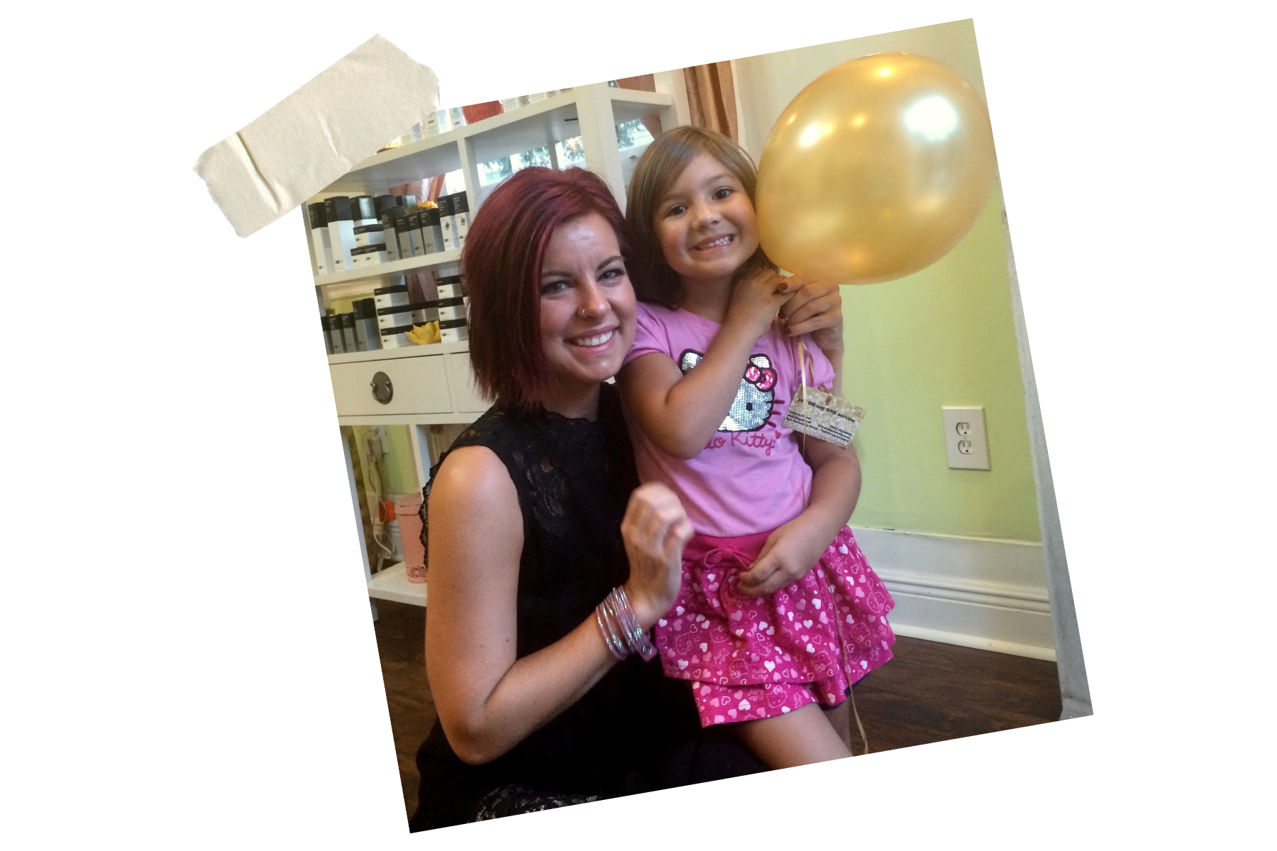 A woman with red hair and a young girl holding a gold balloon, both smiling and sitting indoors.