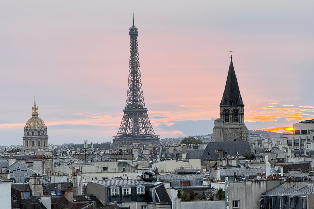 Paris city skyline at sunset featuring the Eiffel Tower, a church steeple, and a domed building in the background.