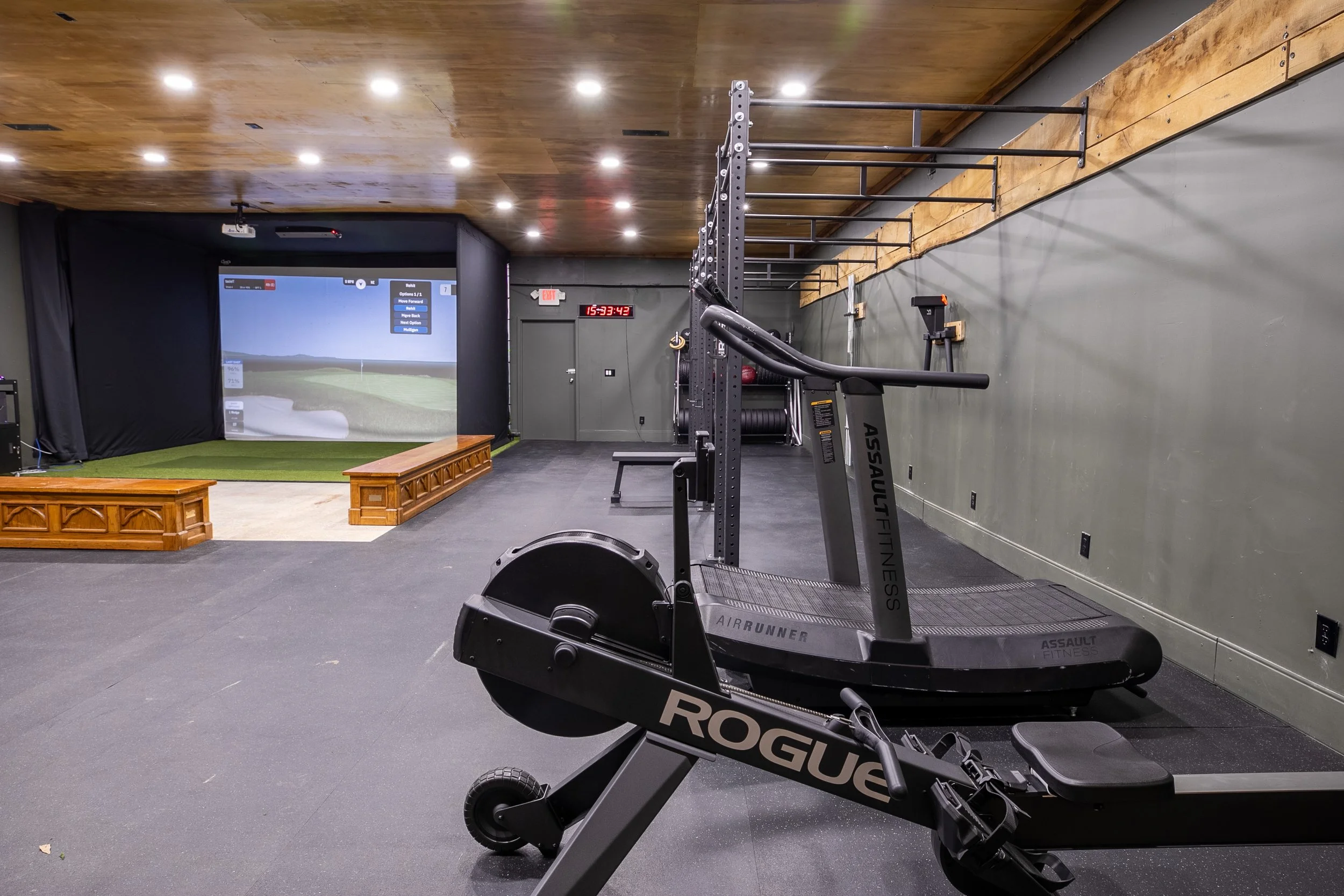 Cardio training equipment in an open gym space with an indoor golf simulator