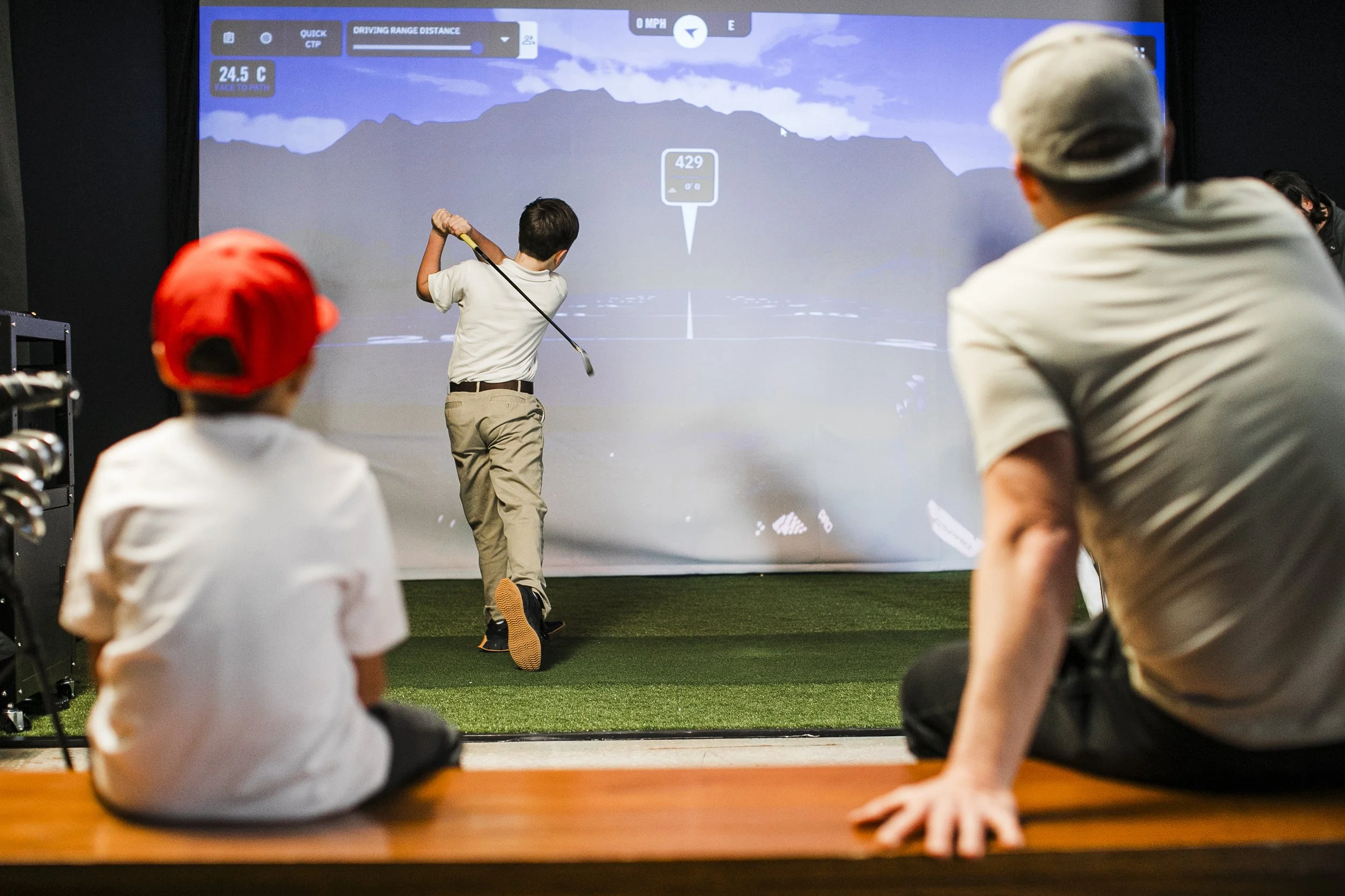 Two young boys swinging golf clubs and training at a golf simulator club in Fairburn Georgia