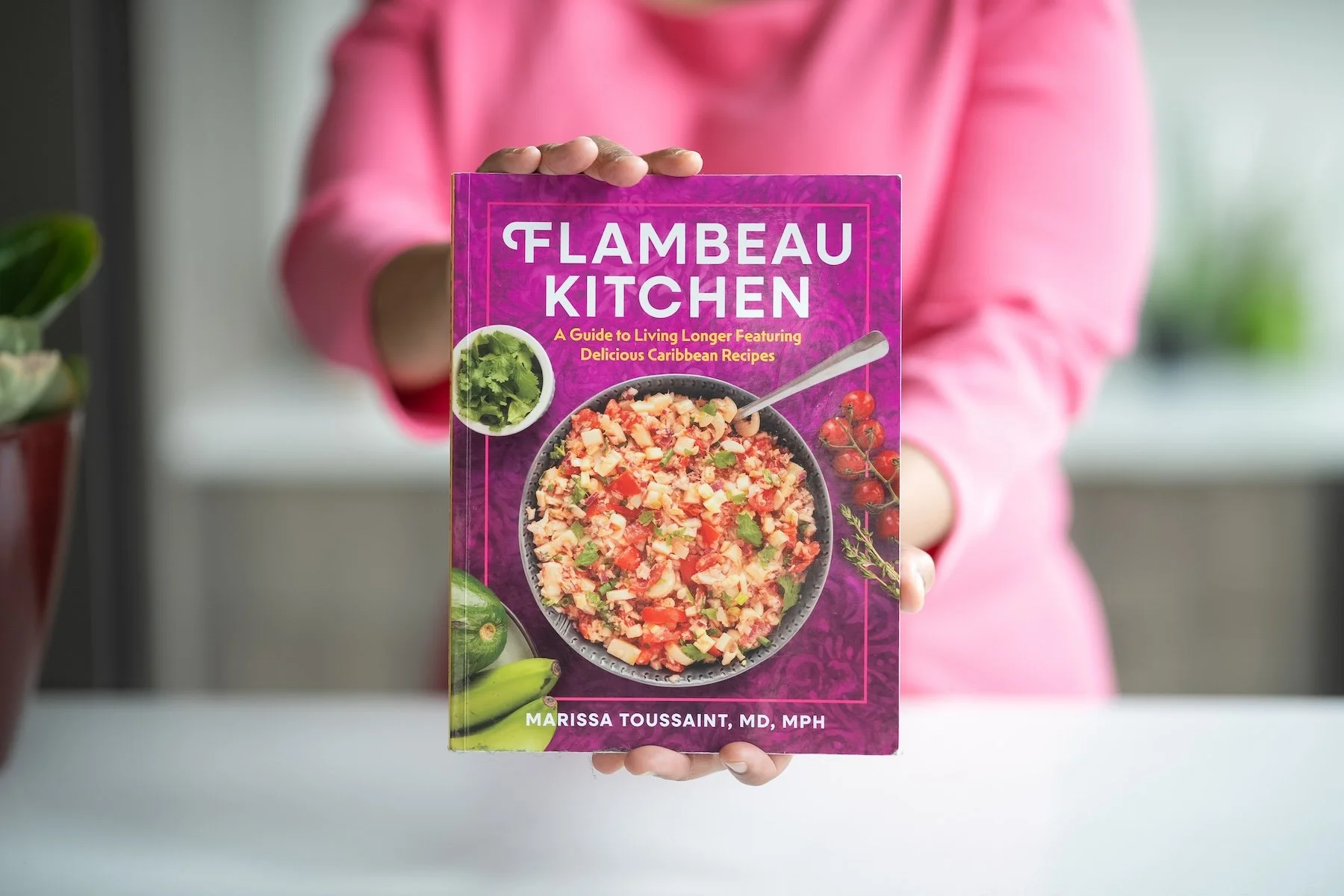 Closeup of Dr. Marissa Toussaint's hands presenting the front cover of the Caribbean cookbook Flambeau Kitchen