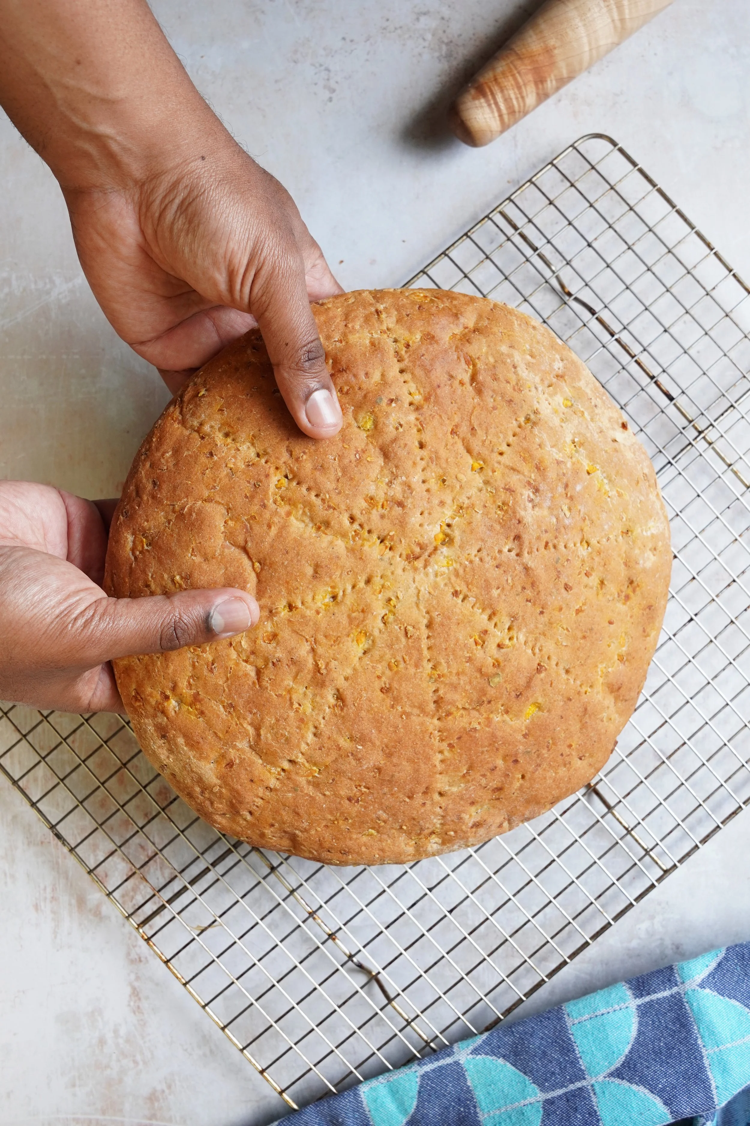 Two hands holding a circular loaf of whole wheat pumpkin bread