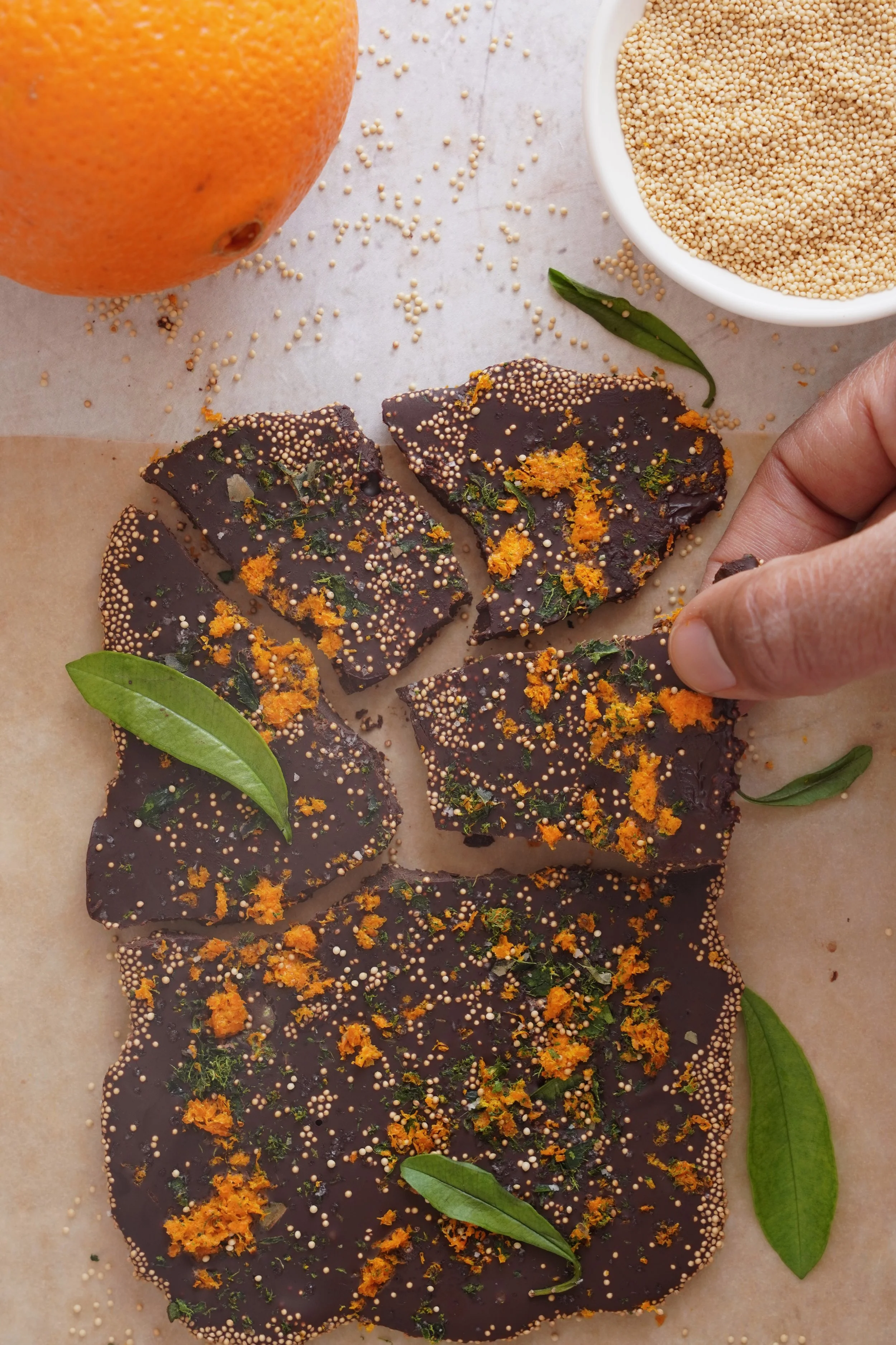 Dark Chocolate Bark with Citrus Crunch surrounded by an orange and a bowl of sesame seeds