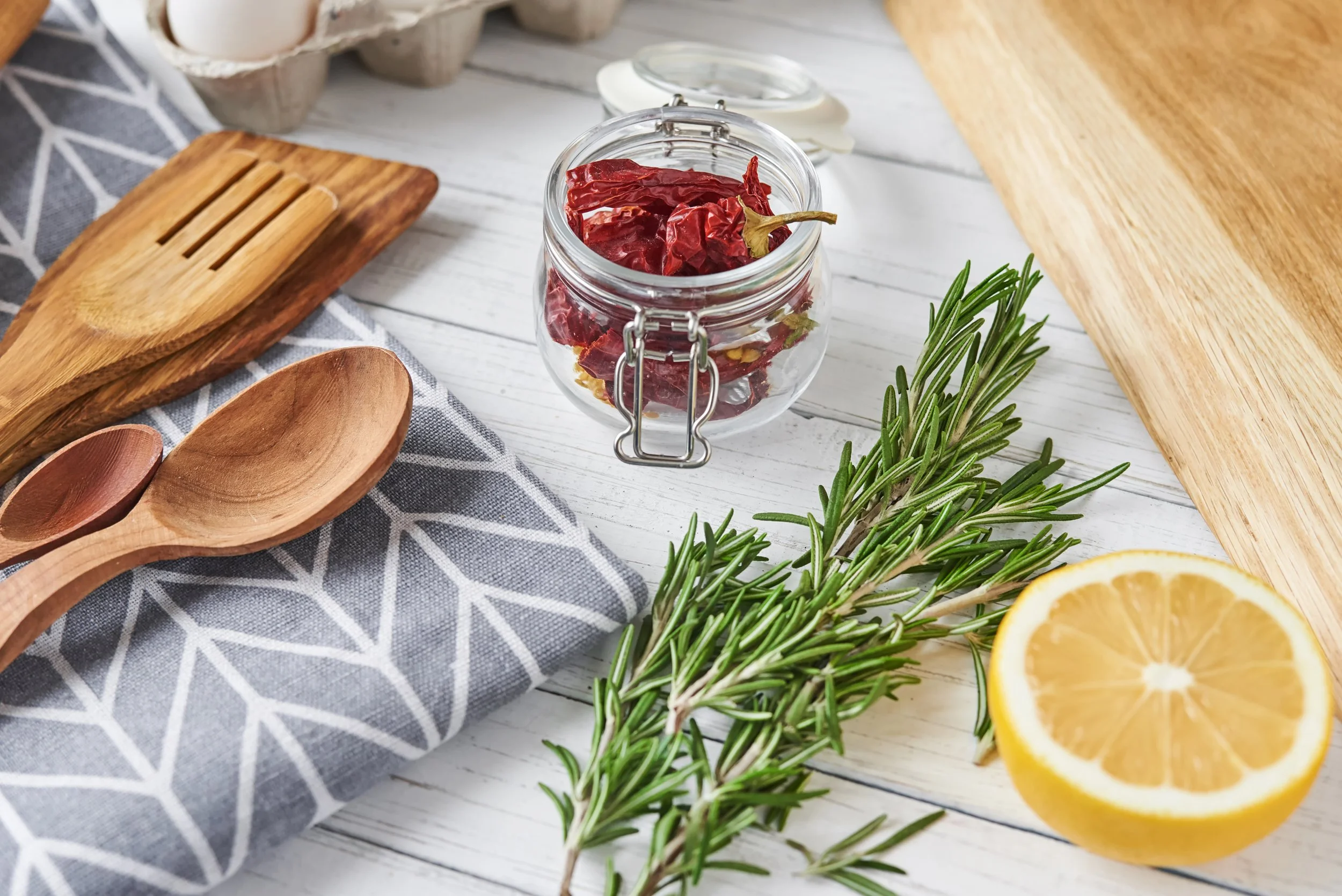 Wooden Kitchen utensils, a sprig of rosemary, half a lemon and a jar of red peppers