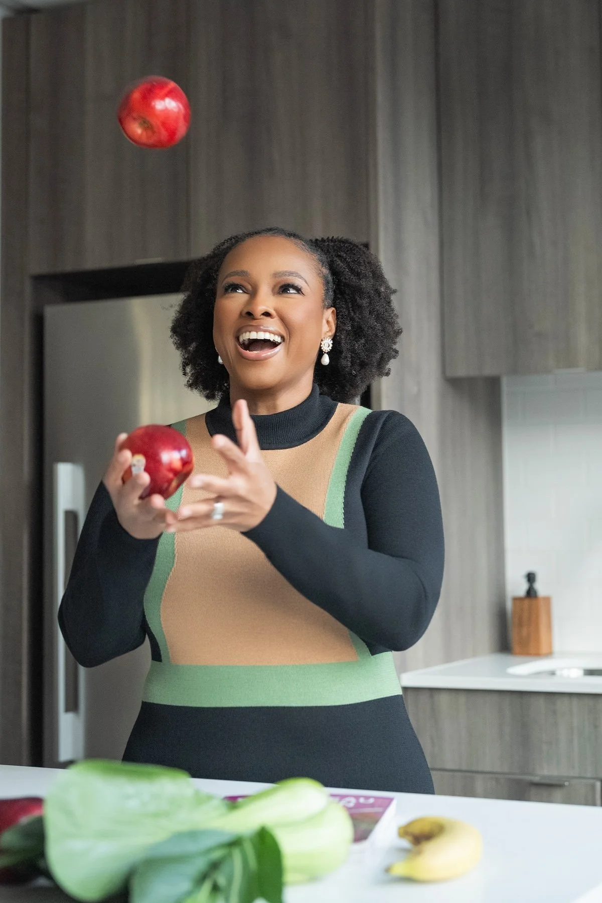 Dr. Marissa Toussaint, MD in a kitchen laughing while juggling red apples in the air