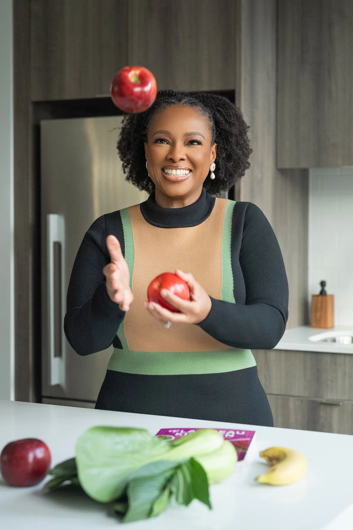 Dr. Marissa Toussaint, MD in a kitchen smiling while juggling red apples in the air