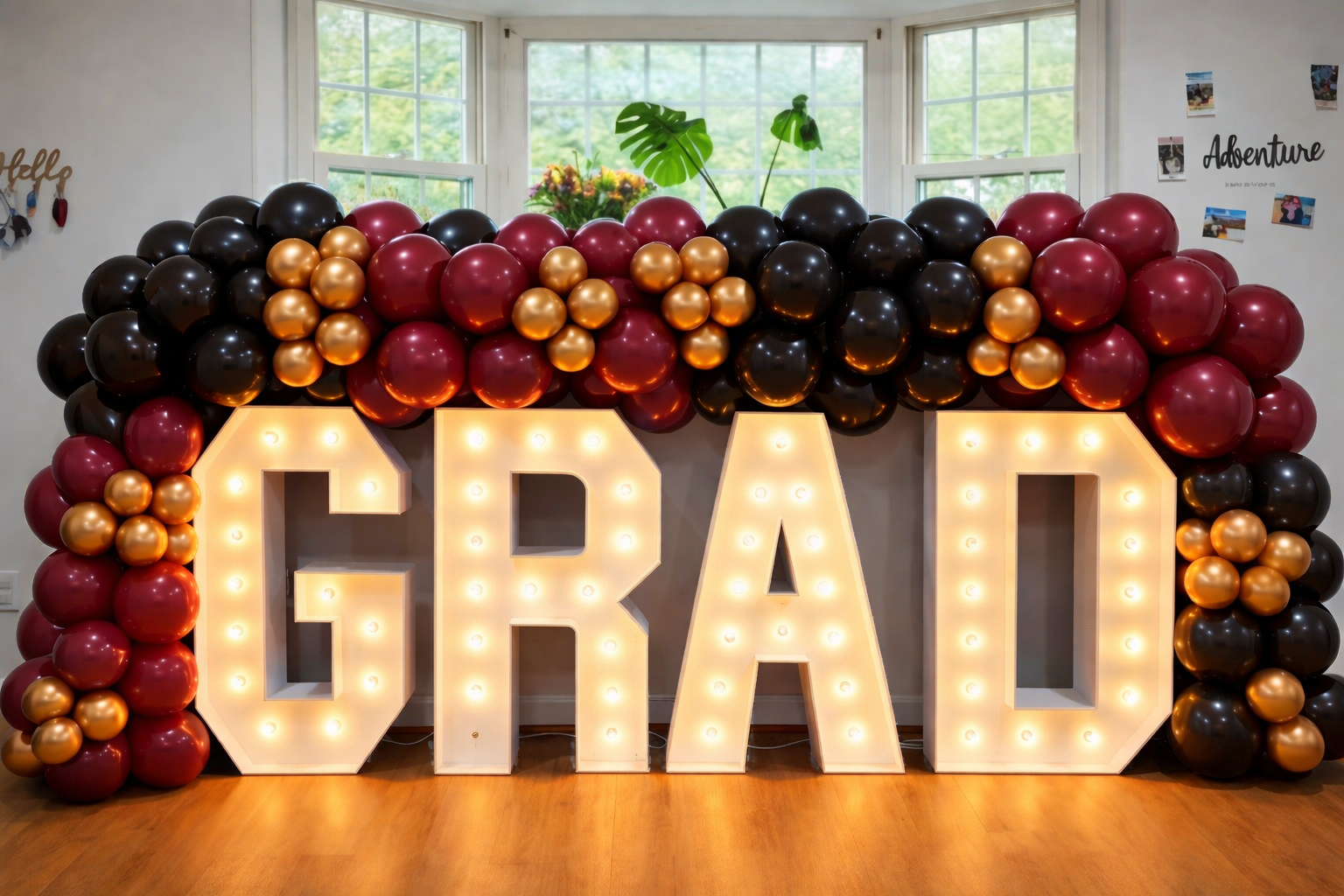 A heart-shaped balloon display with red, black, and gold balloons and large illuminated letters spelling 'GRAD' in front, decorated for a graduation celebration.